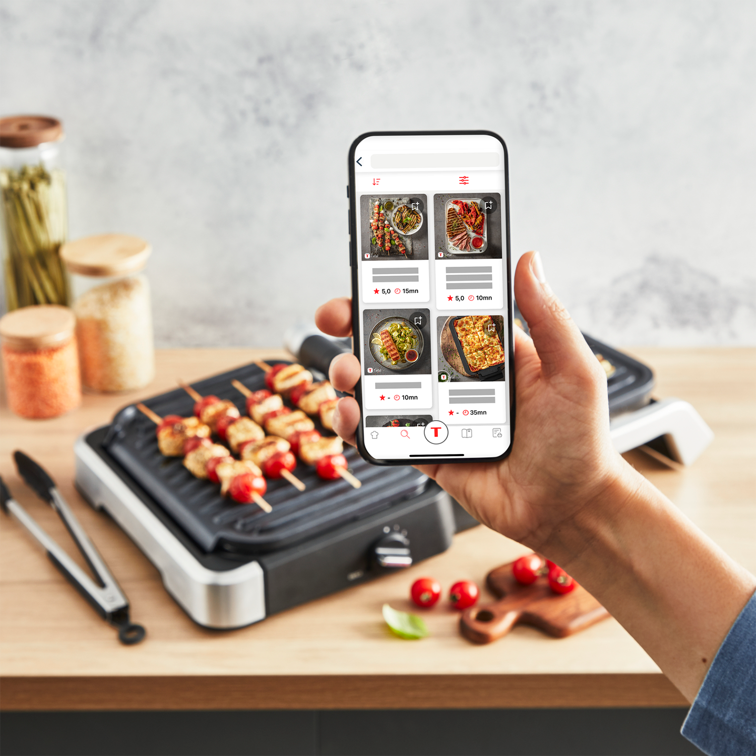 A person using a phone displaying food recipes next to a grill with skewers.