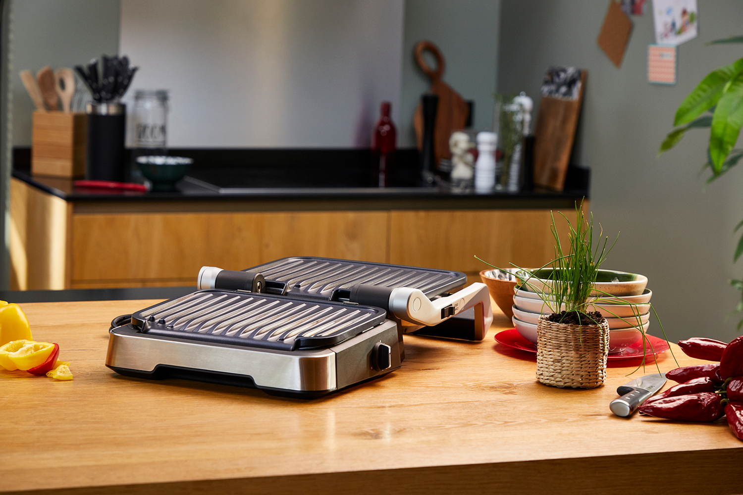 Two electric grills on a wooden table, with a kitchen background.