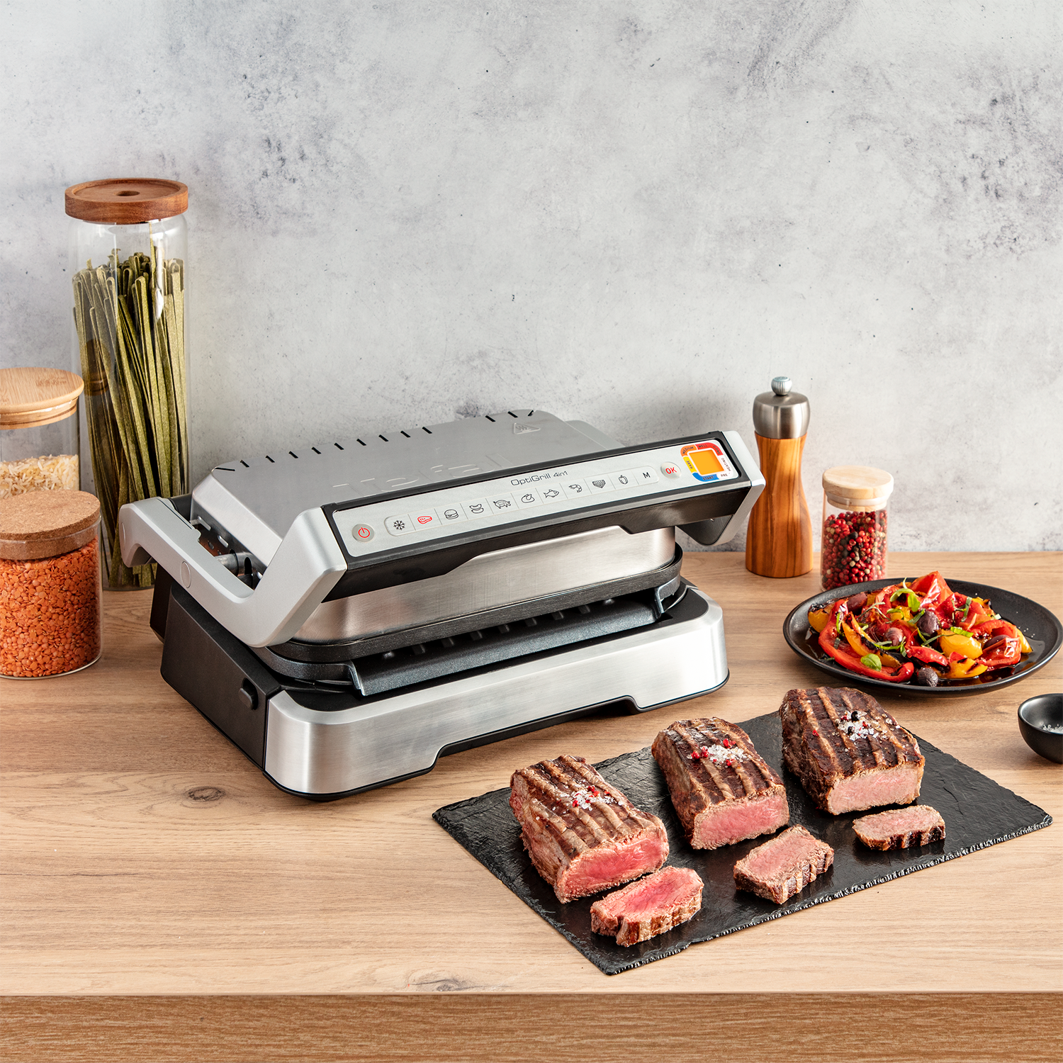Een tafelgrill met gebakken steaks, groenten en kruiden op een houten oppervlak.
