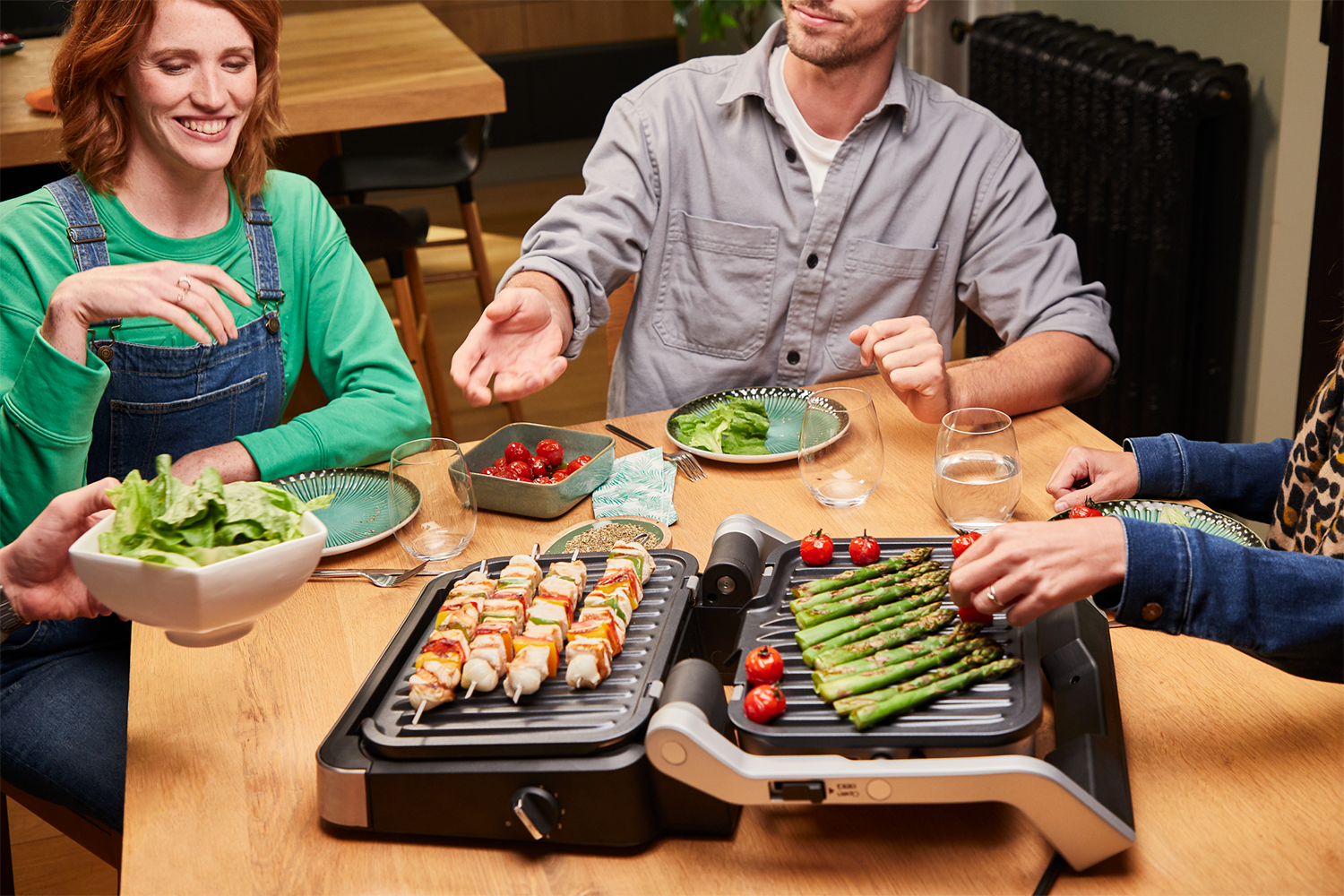 Mensen aan tafel die eten grillen. Inclusief spiesjes, asperges en tomaten.