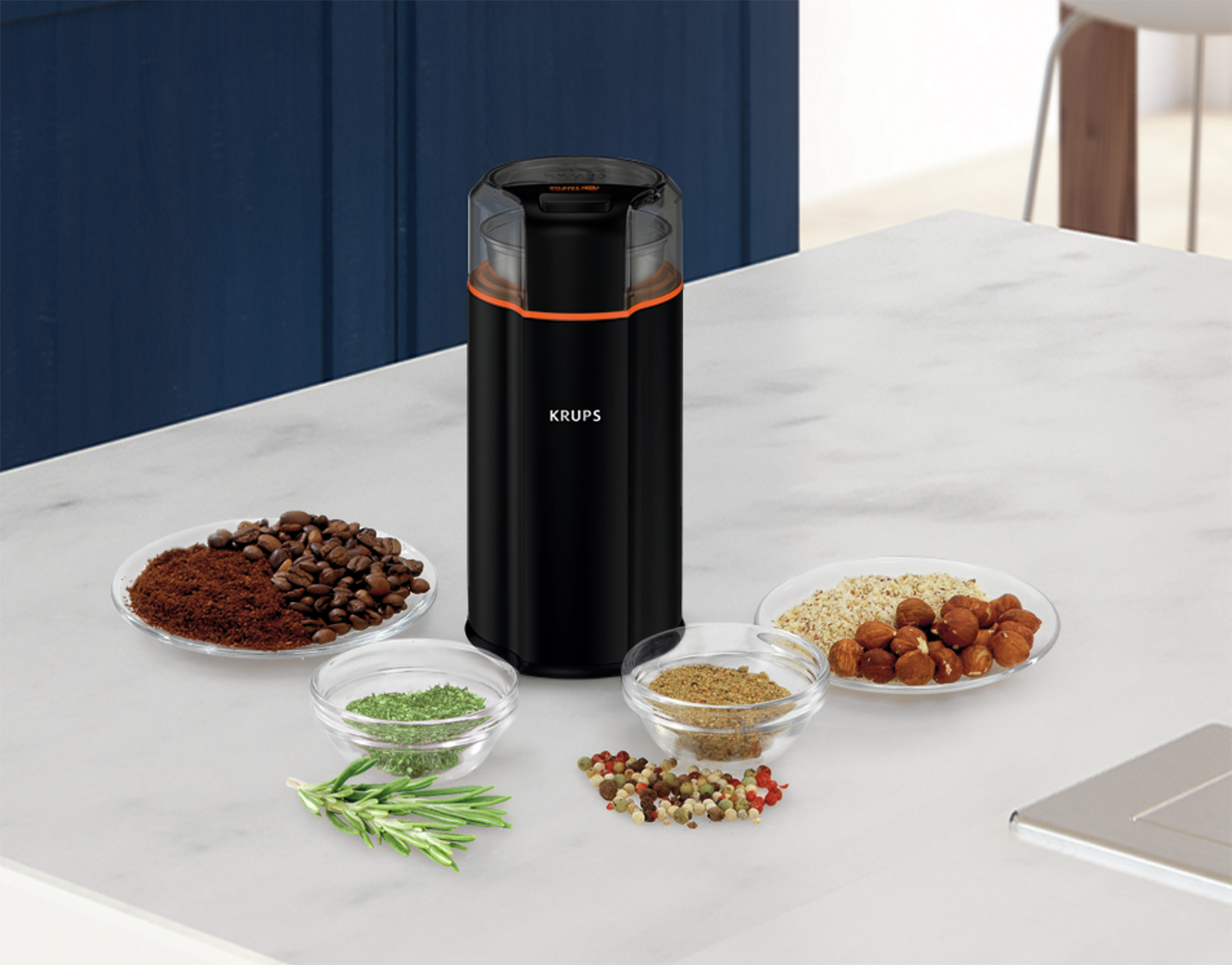 A black coffee grinder with coffee beans, ground coffee, and spices on a counter.