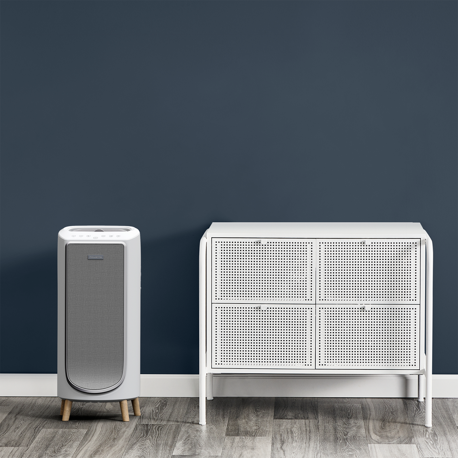 A modern white air purifier and cabinet against a dark blue wall.
