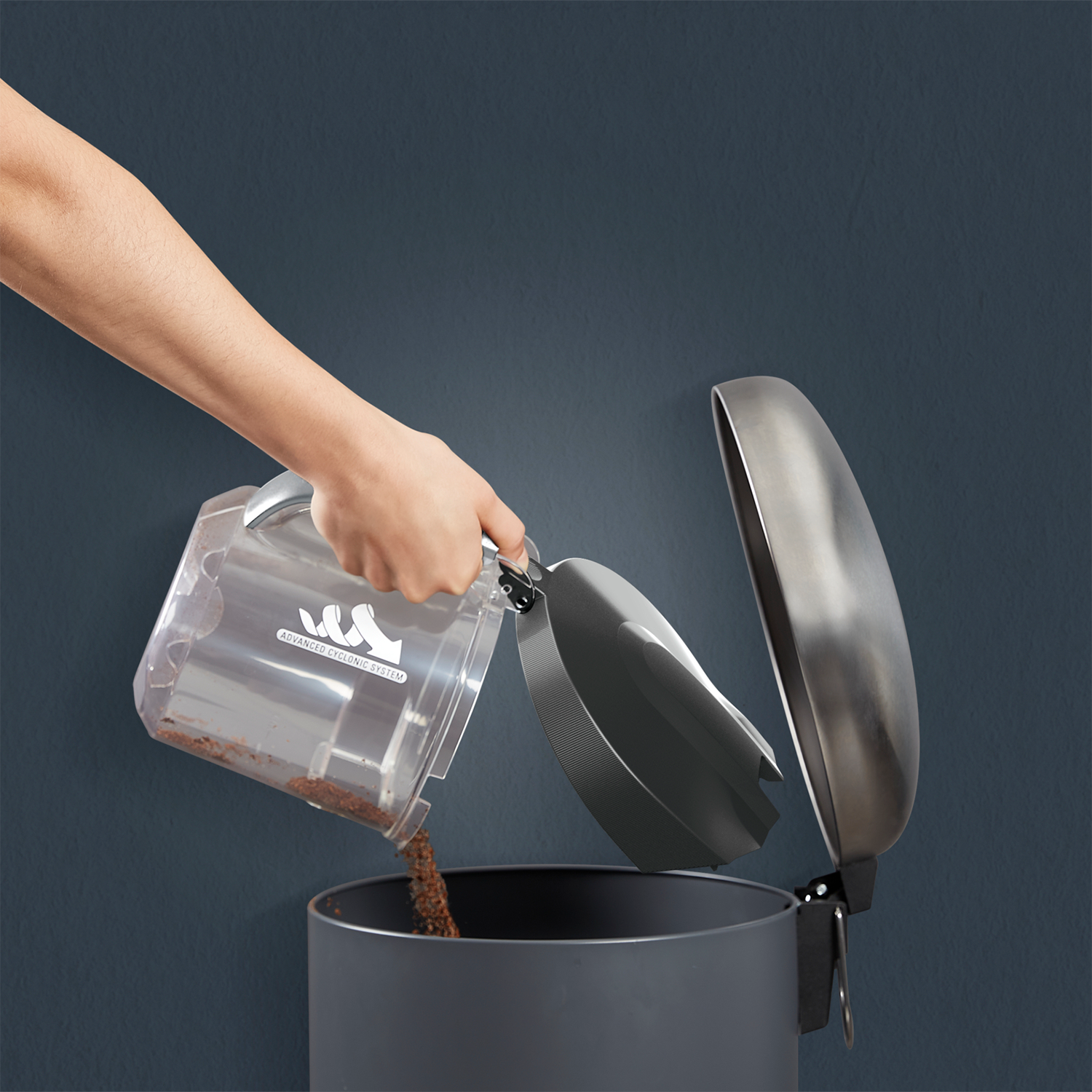 A hand empties a vacuum cleaner's bin into a gray trash can.