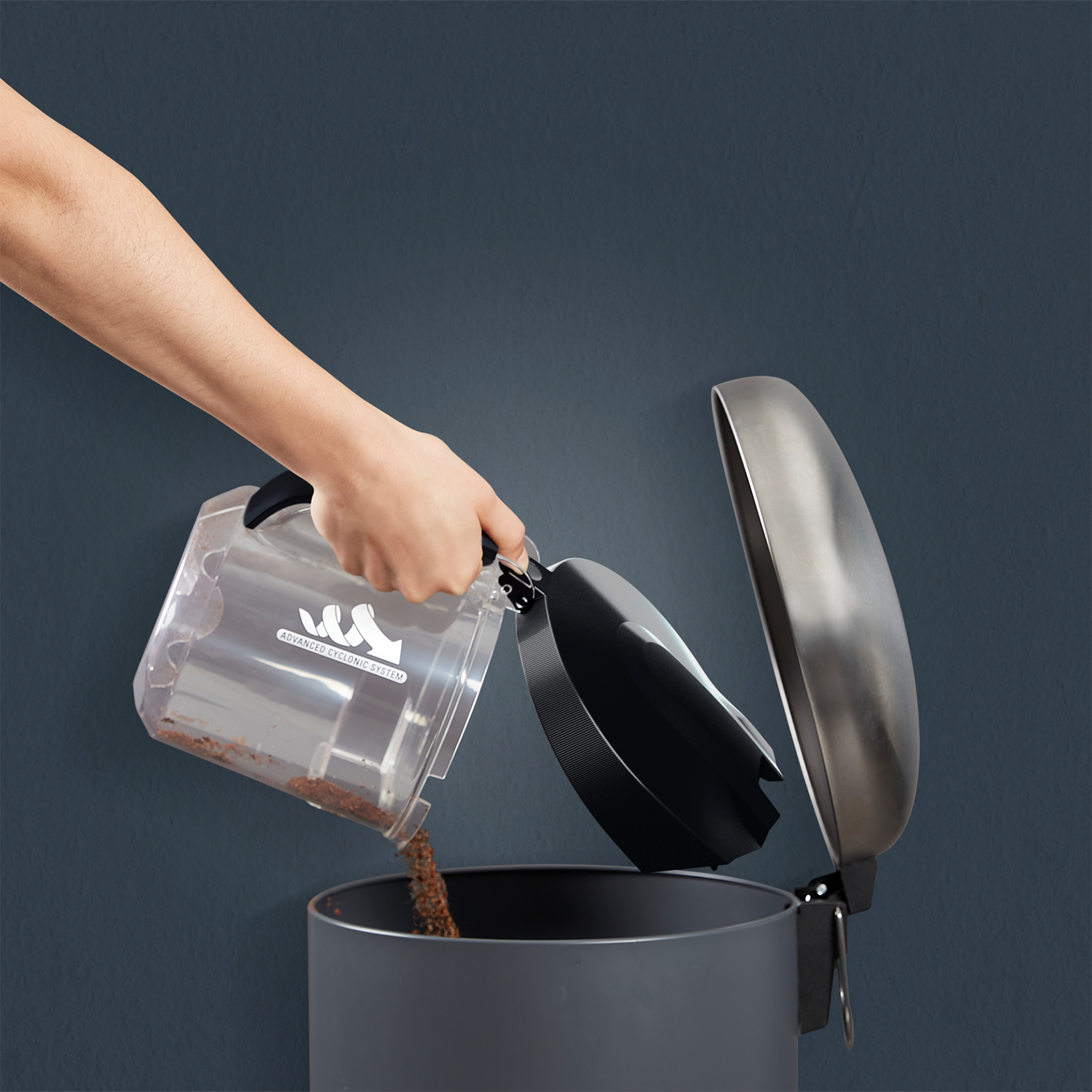 Person emptying a vacuum cleaner container into a trash bin. Brown debris visible.
