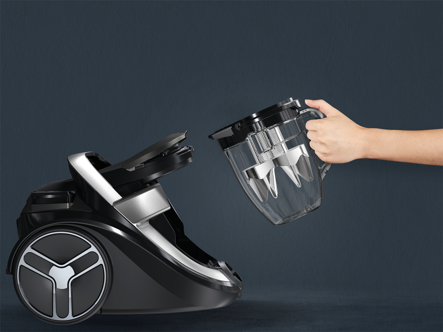 Vacuum cleaner with a hand removing a dust container. Black and silver.
