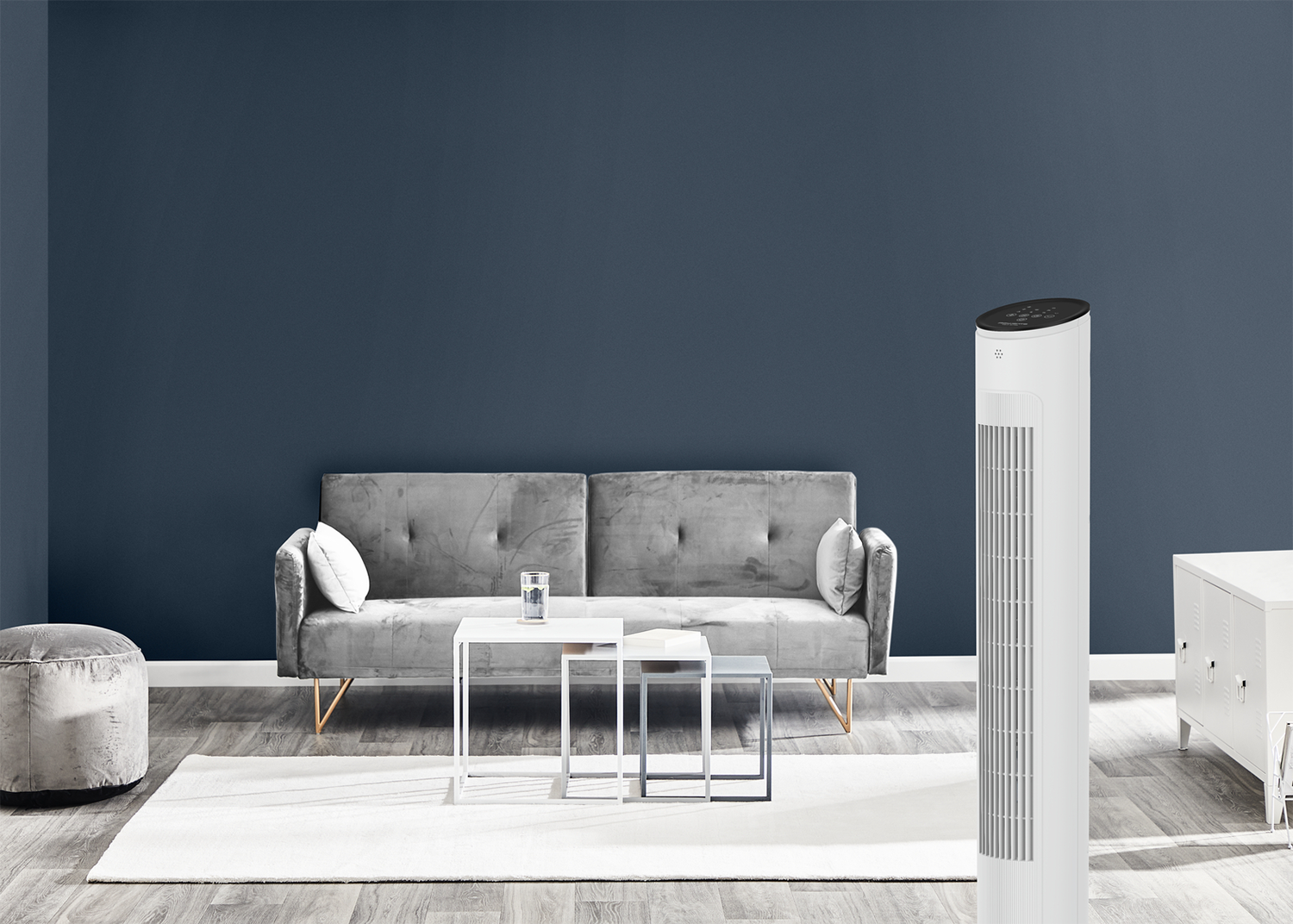 Salon moderne avec un canapé gris, des tables blanches, un ventilateur et un mur bleu. Un tapis est sur le sol en bois.