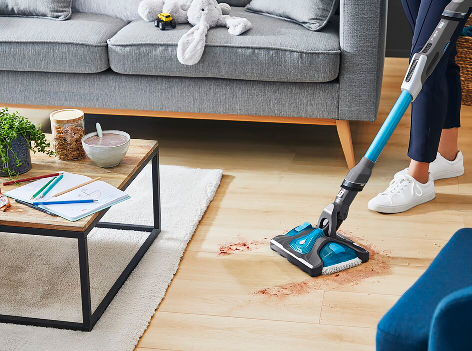 A person vacuuming a wooden floor in a living room.
