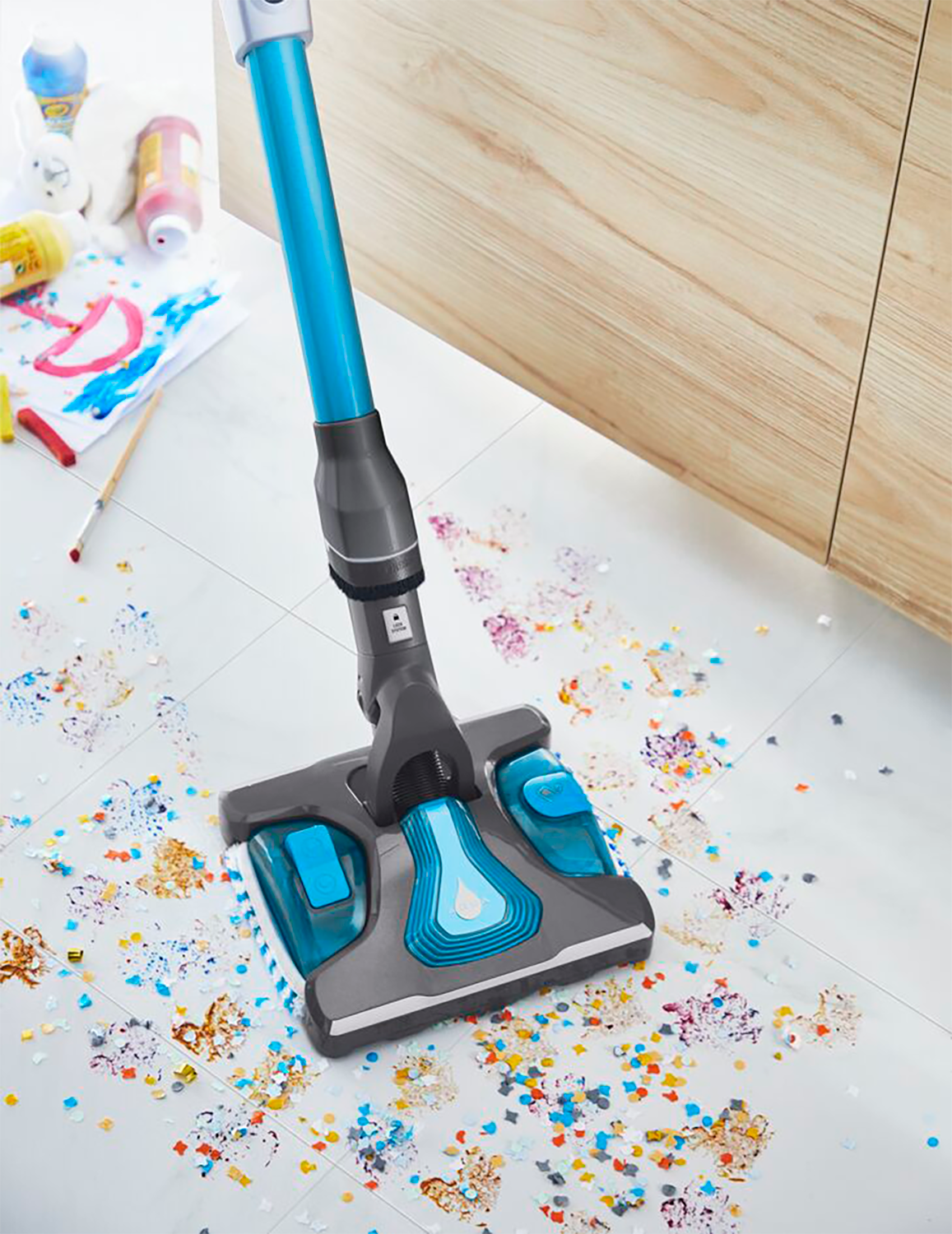 Vacuum cleaner cleaning confetti and small colorful paper shapes on floor.
