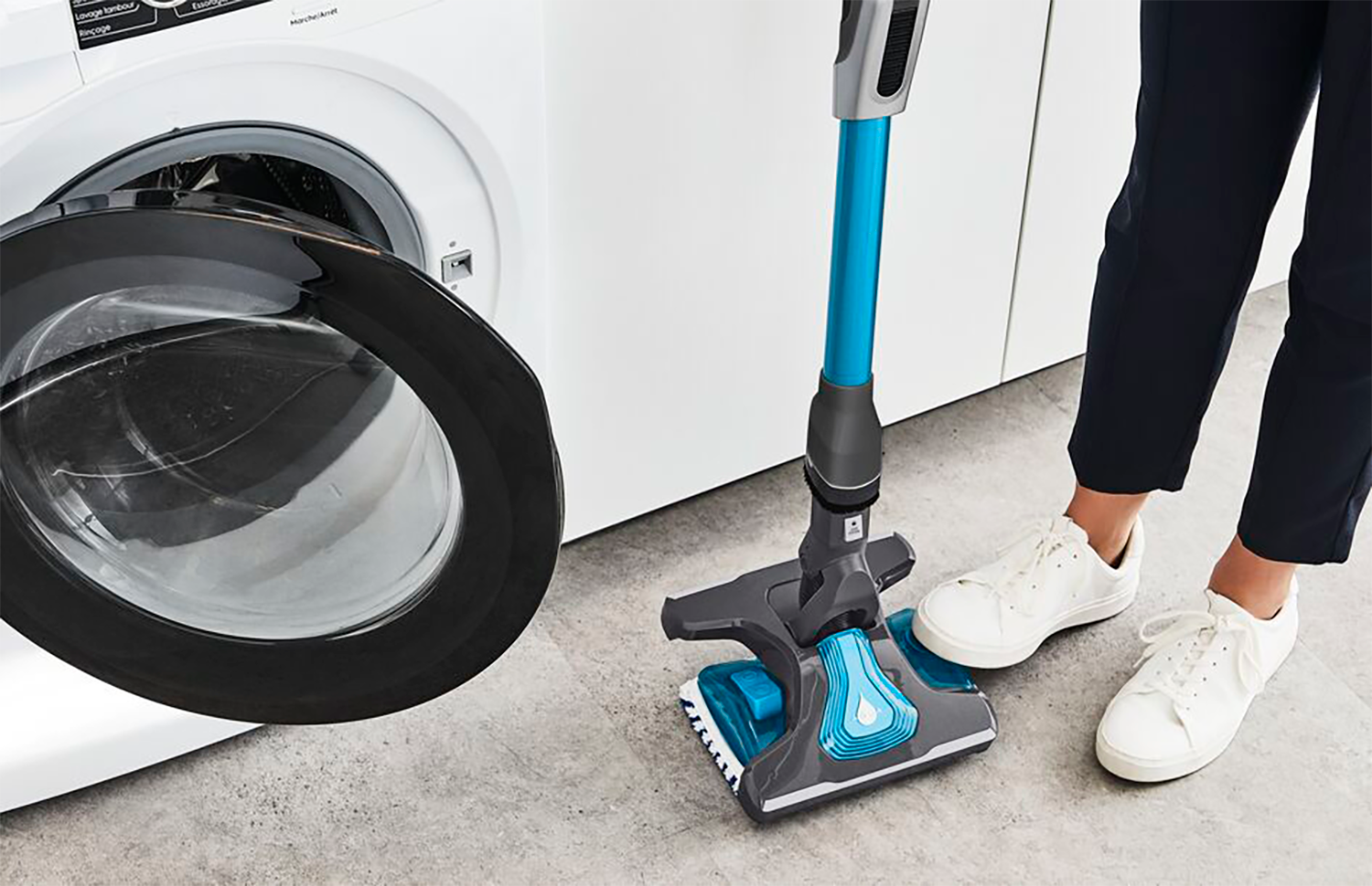 A person's feet, and a vacuum cleaner. The vacuum cleaner is blue and black.