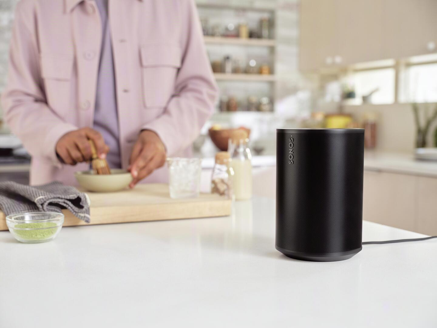 Altavoz negro en mostrador blanco, una persona cocina.
