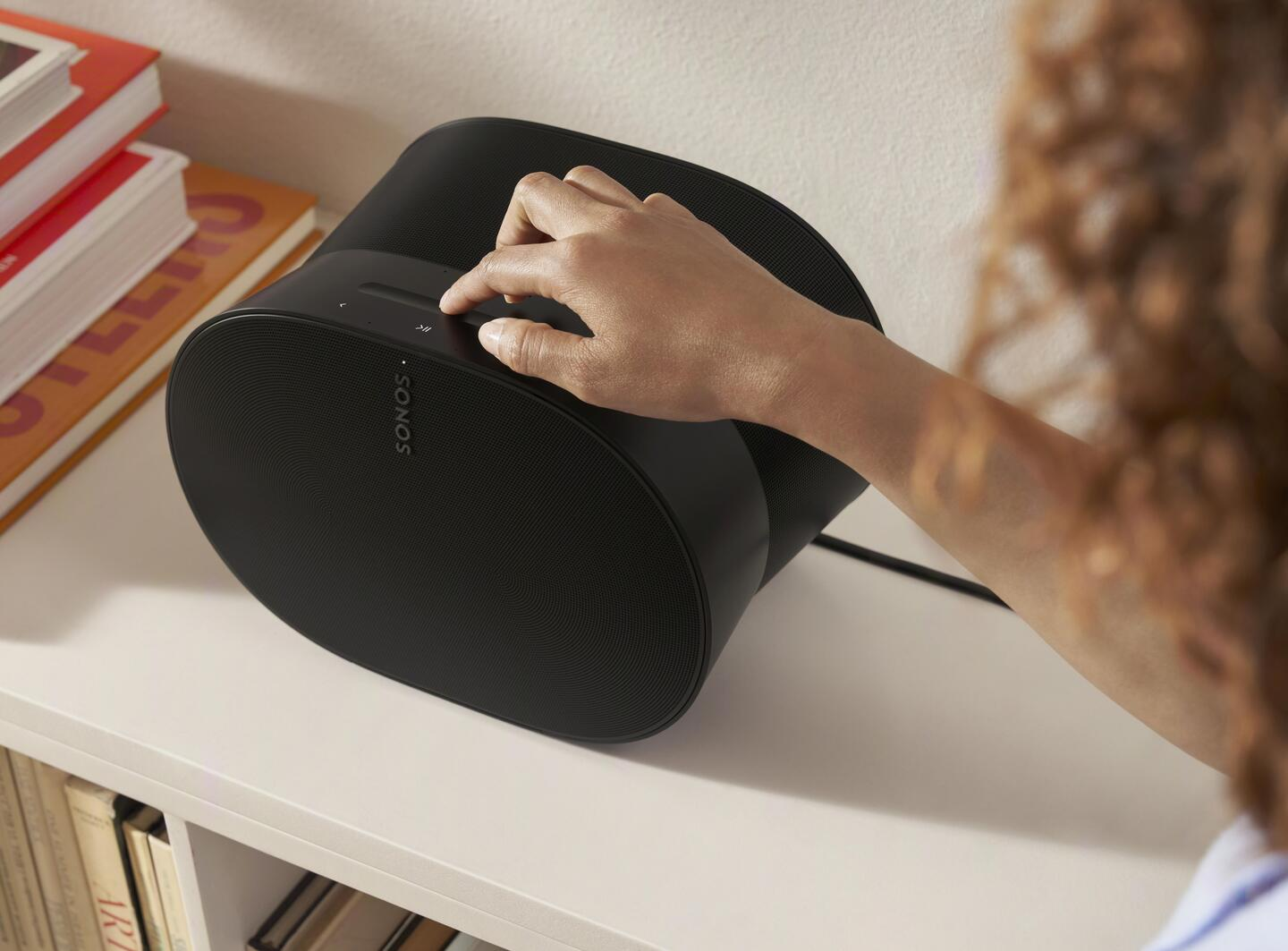 Persona ajustando el volumen en un altavoz Sonos negro en una estantería.