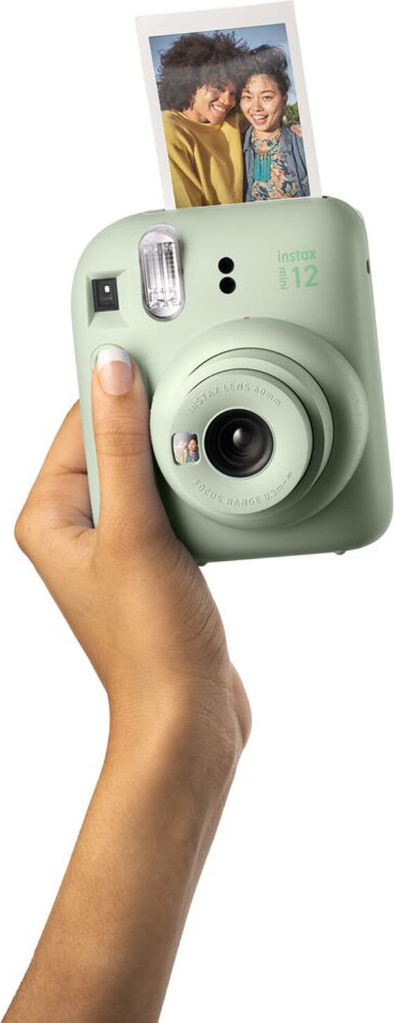 Hand hält grüne Instax Mini 12 Kamera, mit herauskommendem Foto.