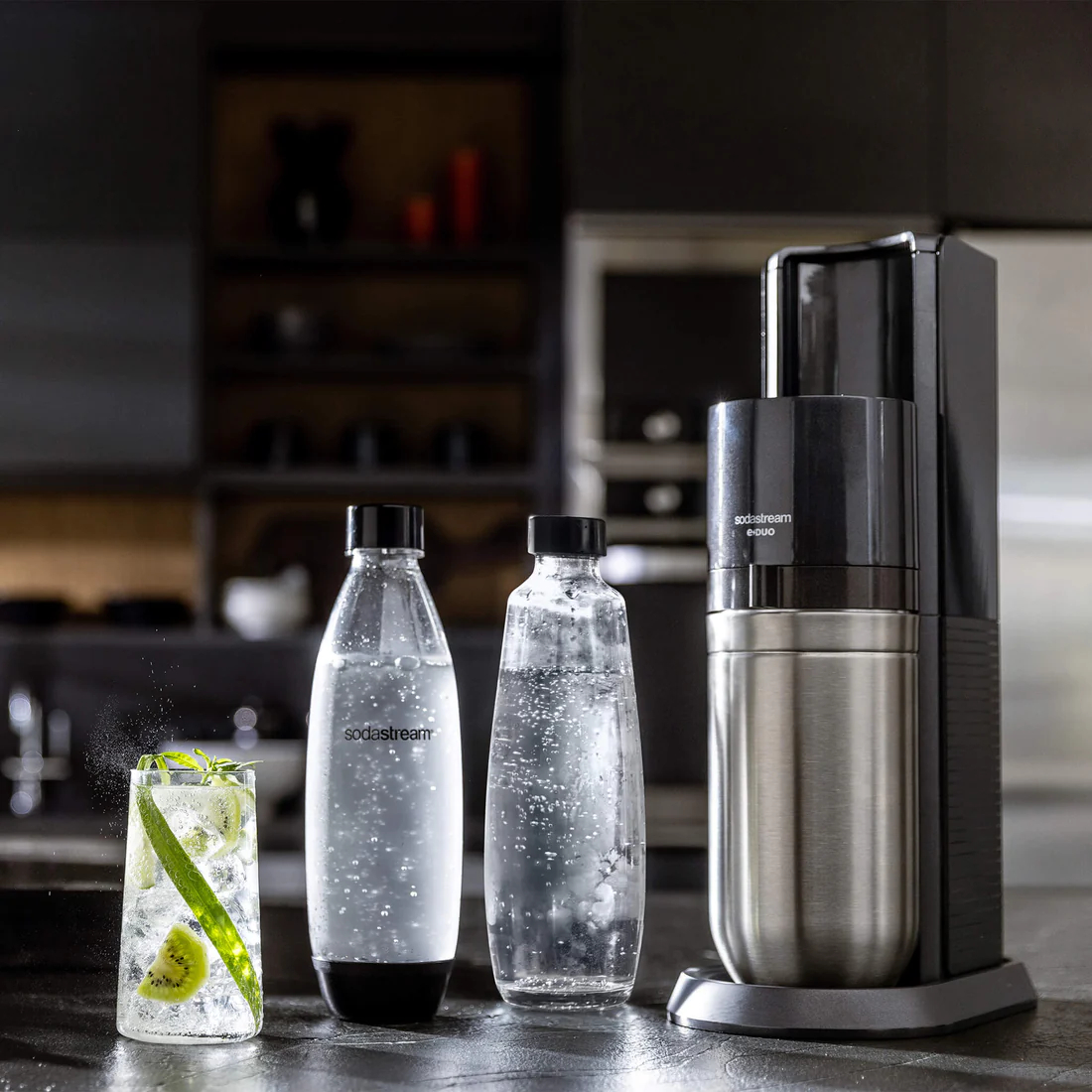 Eine SodaStream e-DUO Maschine mit zwei Flaschen und einem Glas Getränk auf dunkler Oberfläche.