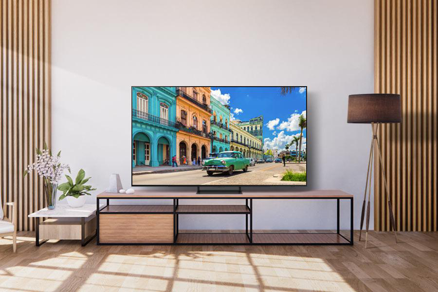 Wohnzimmer mit Fernseher auf Holzständer. Eine Straßenszene auf dem Fernseher und eine Stehlampe rechts.