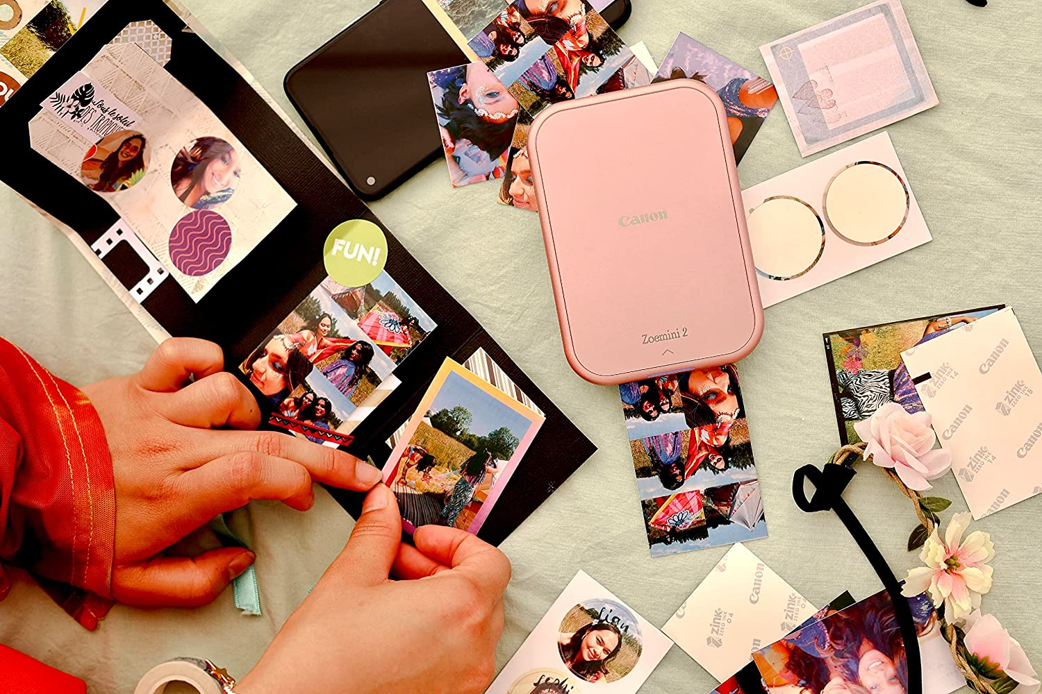 Manos colocando fotos en un álbum de recortes, con una impresora Canon rosa y fotos dispersas.