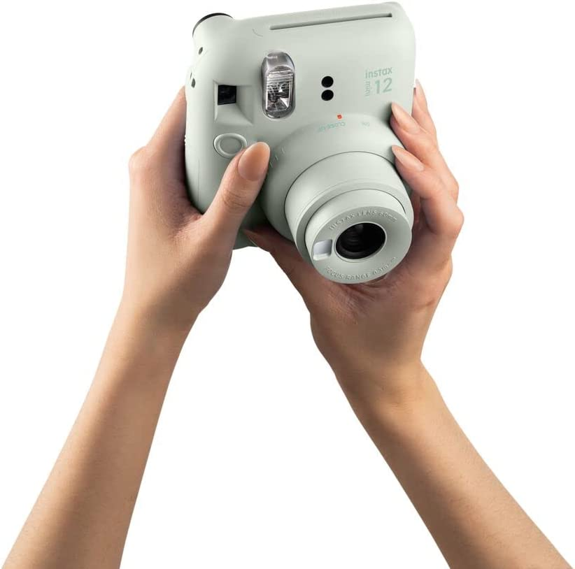 Manos sosteniendo una cámara Instax verde claro, toma de cerca.