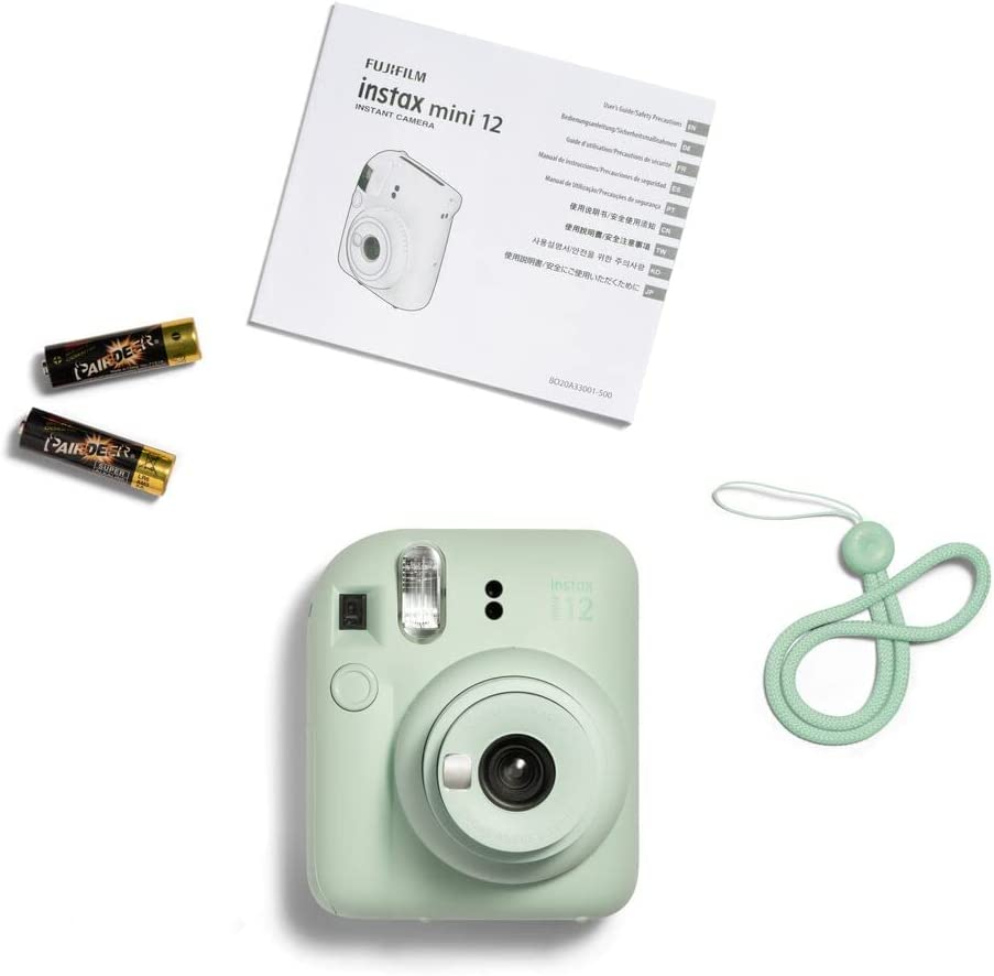 Una cámara Instax Mini 12 verde menta con accesorios sobre una superficie blanca.