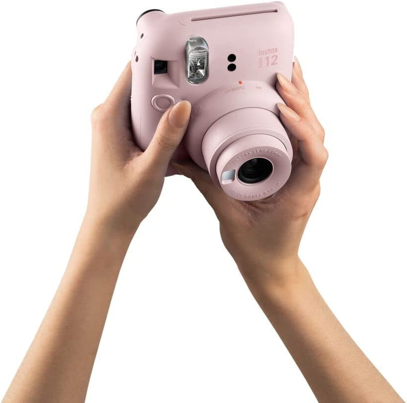 Cámara Instax Mini 12 rosa sostenida con ambas manos, fondo blanco.