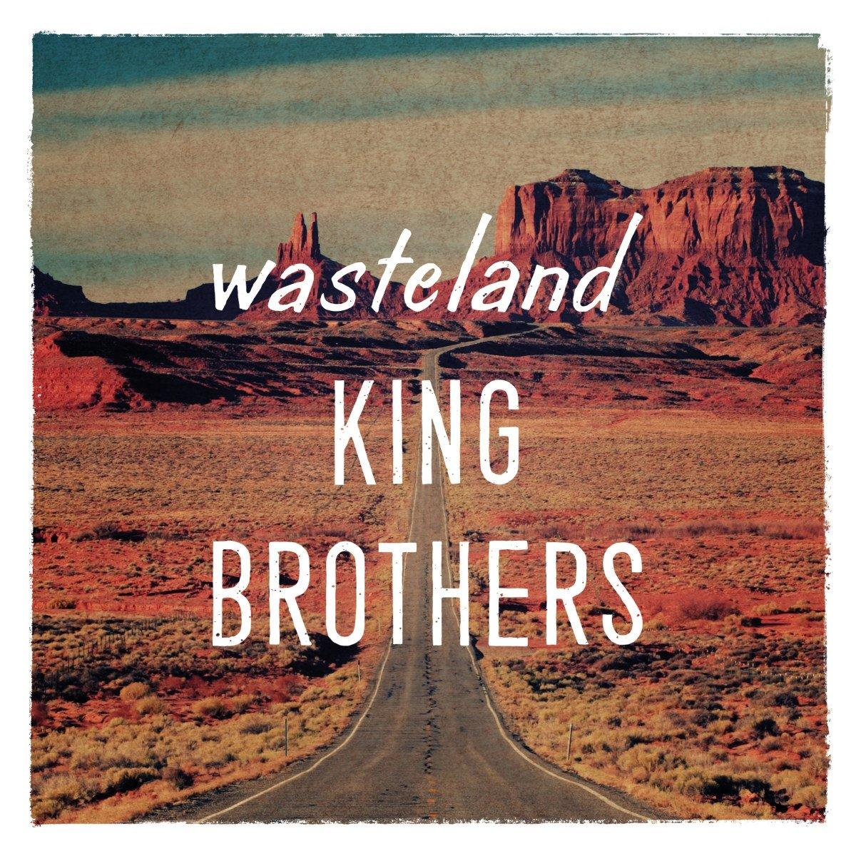 Straße durch Wüstenlandschaft. Textüberlagerung: wasteland KING BROTHERS. Berge im Hintergrund.