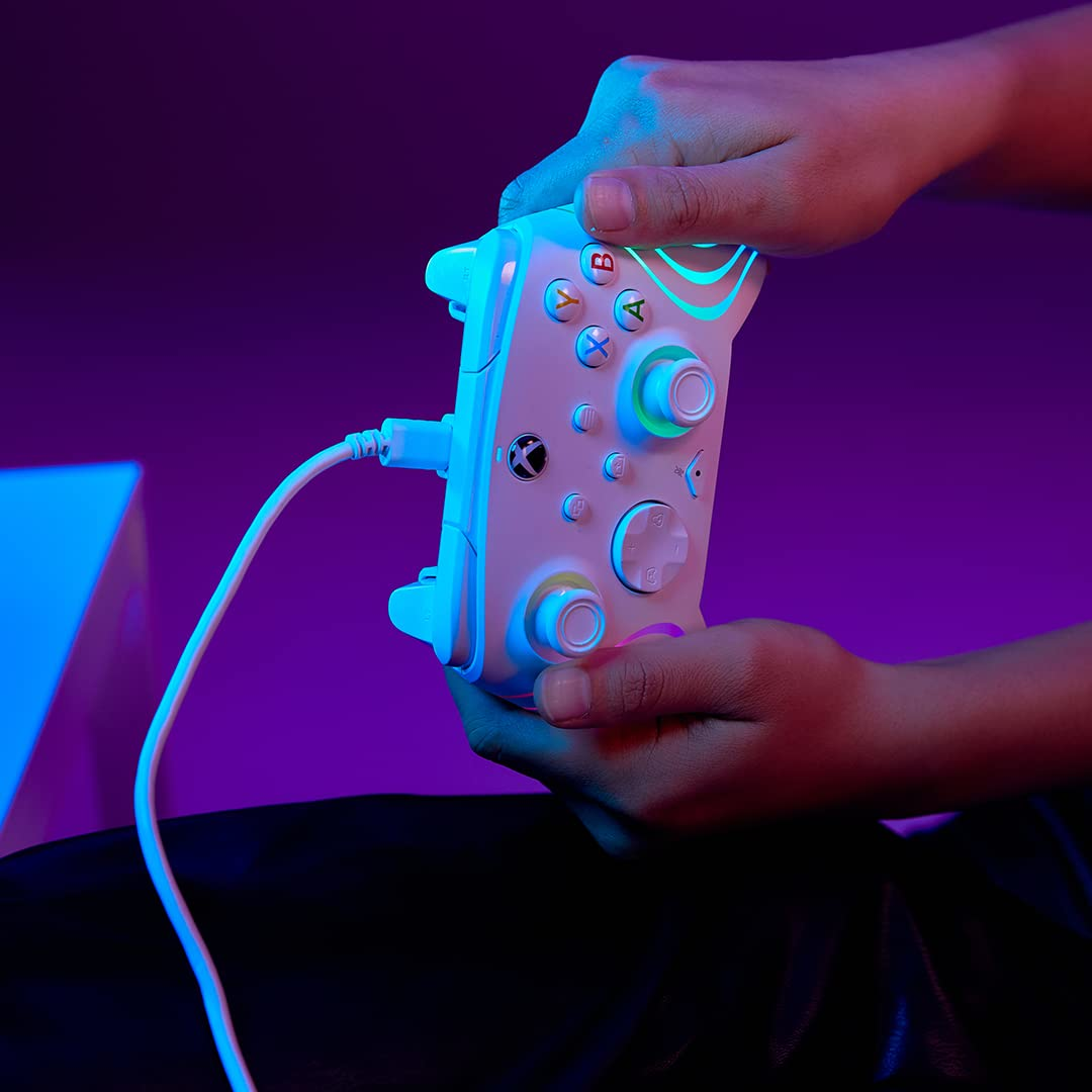 Mani che tengono un controller Xbox bianco e blu, illuminato con luci colorate, su uno sfondo viola.