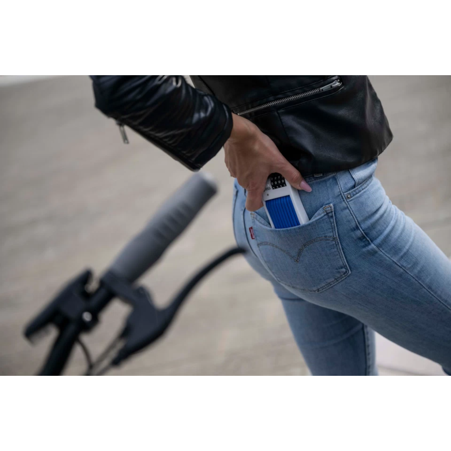 A woman in jeans putting a blue and white device into her back pocket, next to a scooter.