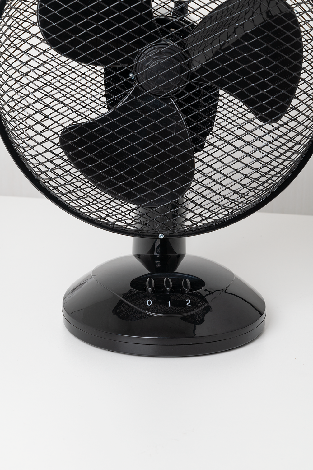 Schwarzer Tischventilator auf weißer Oberfläche. Der Ventilator hat einen Käfig und drei Geschwindigkeitseinstellungen.