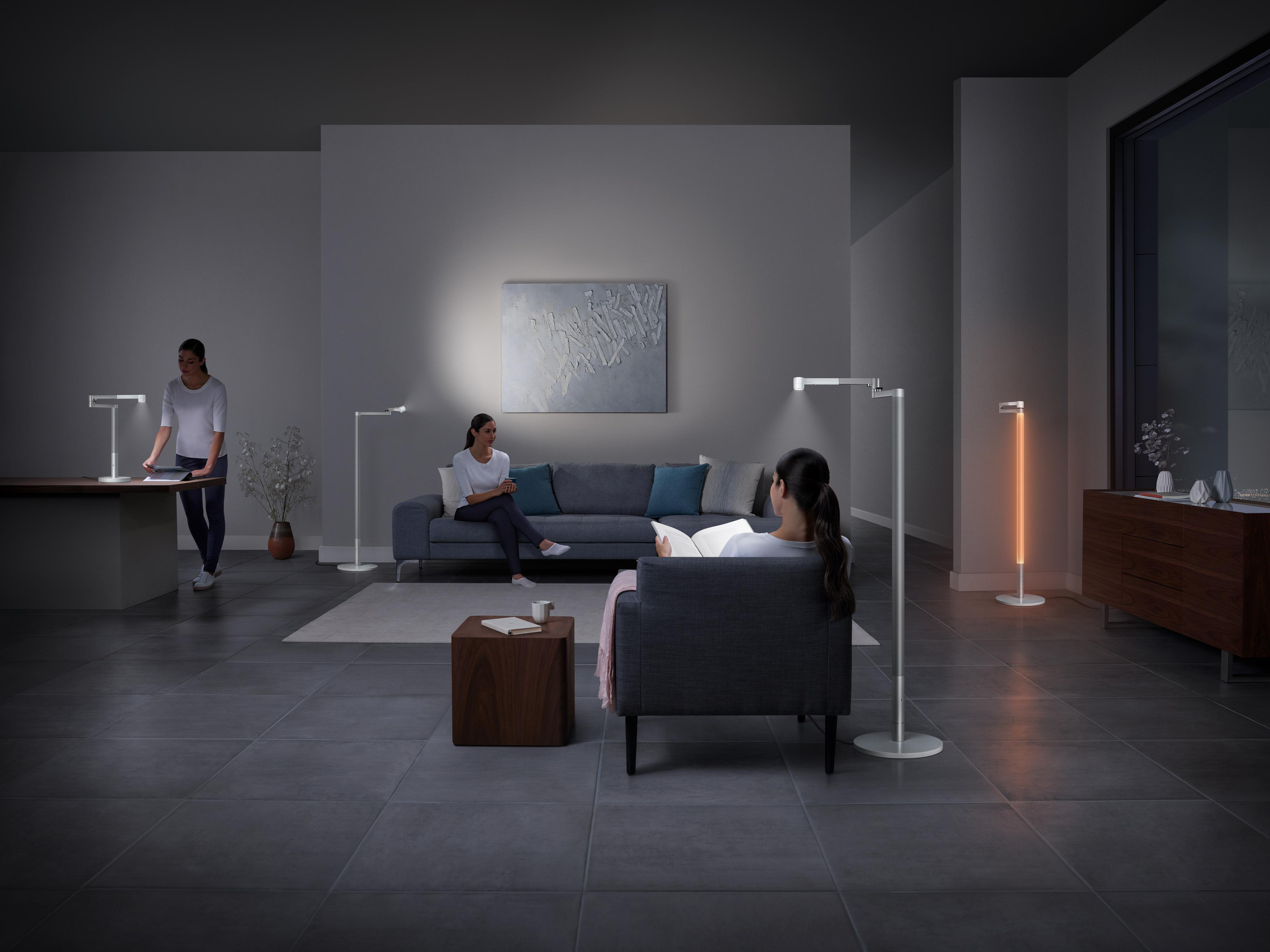 Ein modernes Wohnzimmer mit Personen, Lampen, Sofa und Gemälde an der Wand.