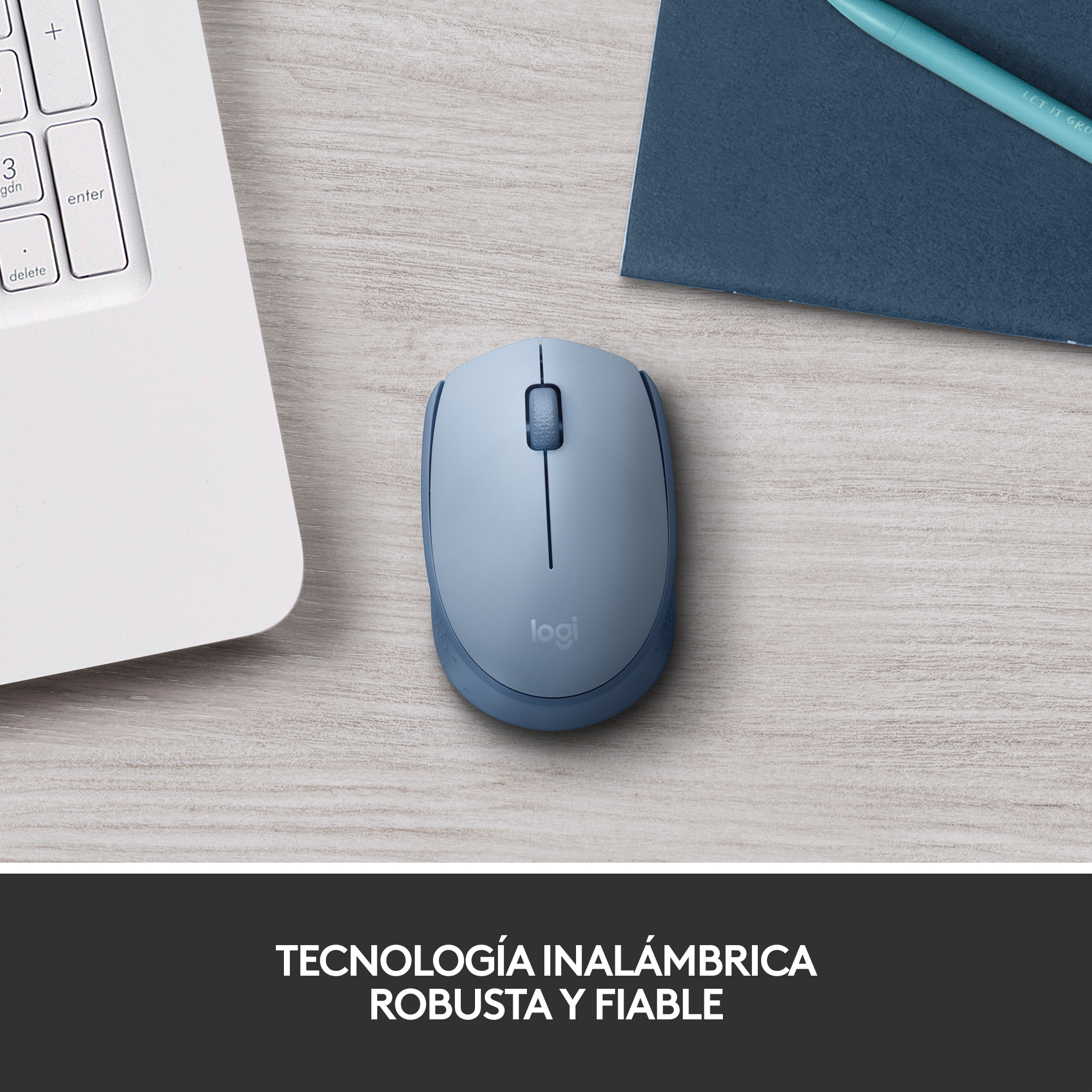 Ratón inalámbrico Logitech azul claro sobre un escritorio de madera con bloc y bolígrafo.