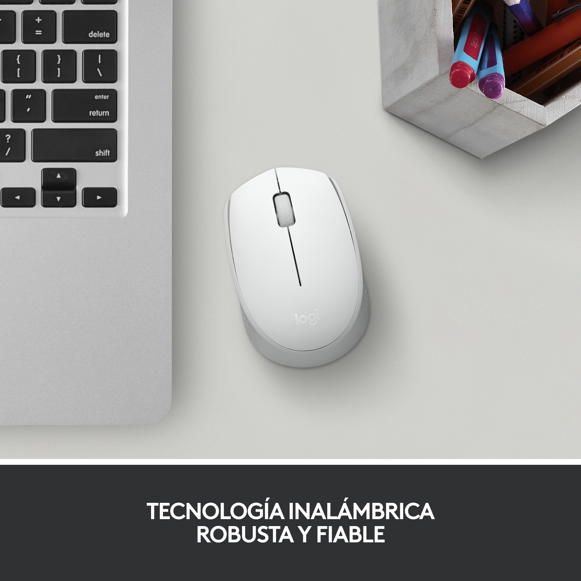Ratón Logitech blanco sobre un escritorio junto a un teclado de portátil y un portalápices.
