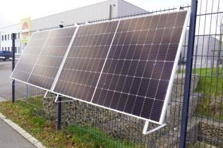 Solarpaneele auf einem Zaun installiert, mit Gebäude im Hintergrund.