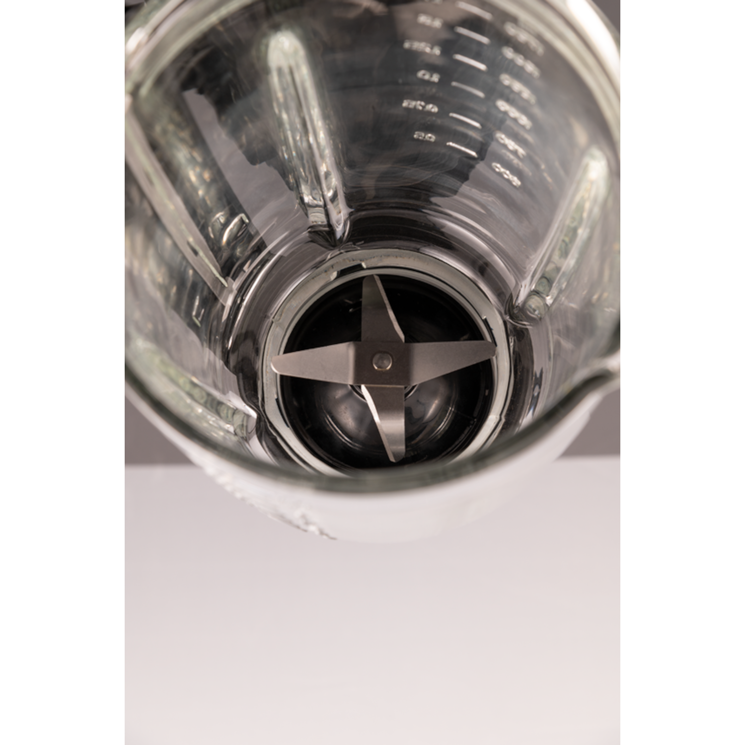 Close-up of a blender's glass container, showing blades. Grey background.