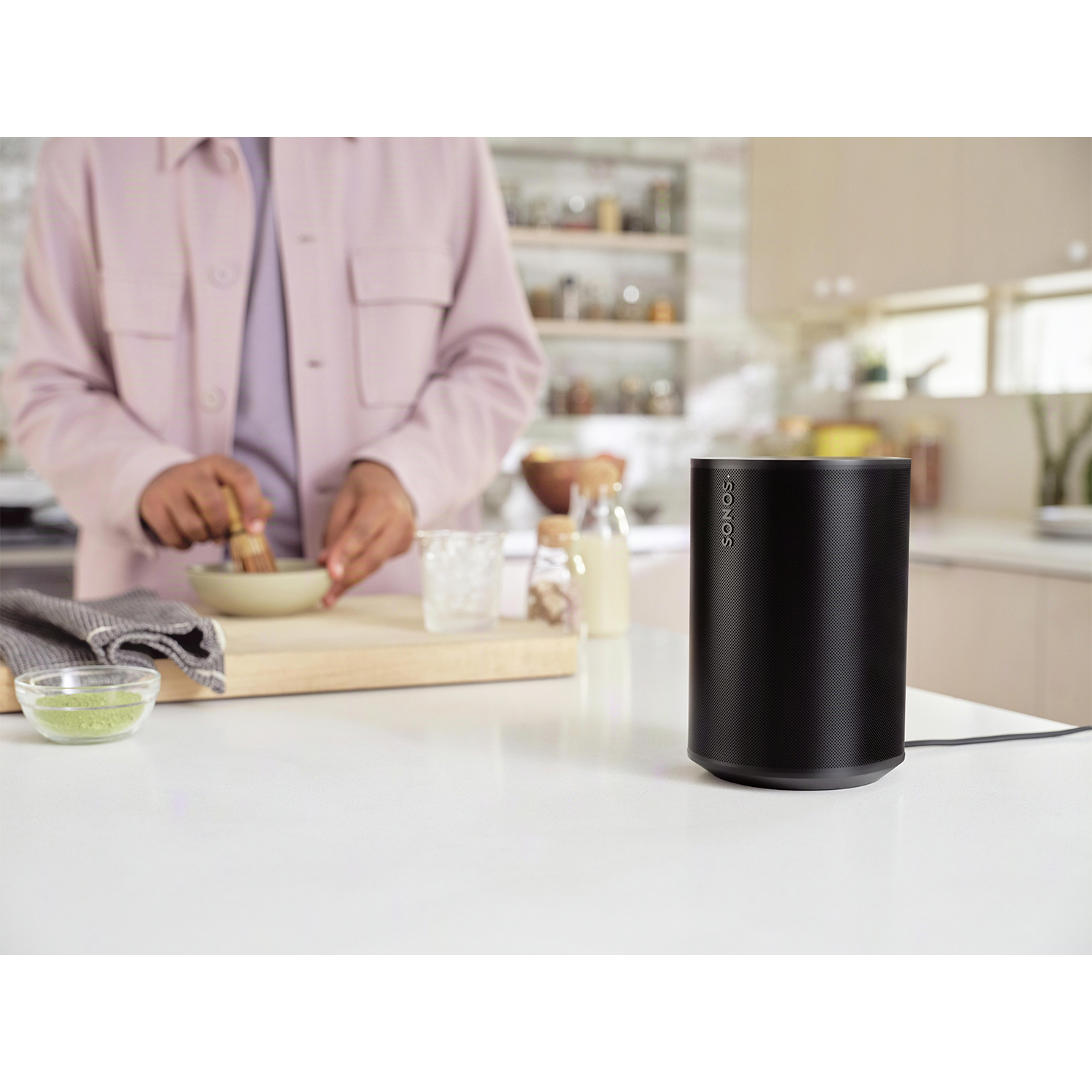 Altoparlante Sonos nero su un bancone bianco, persona che mescola sullo sfondo.
