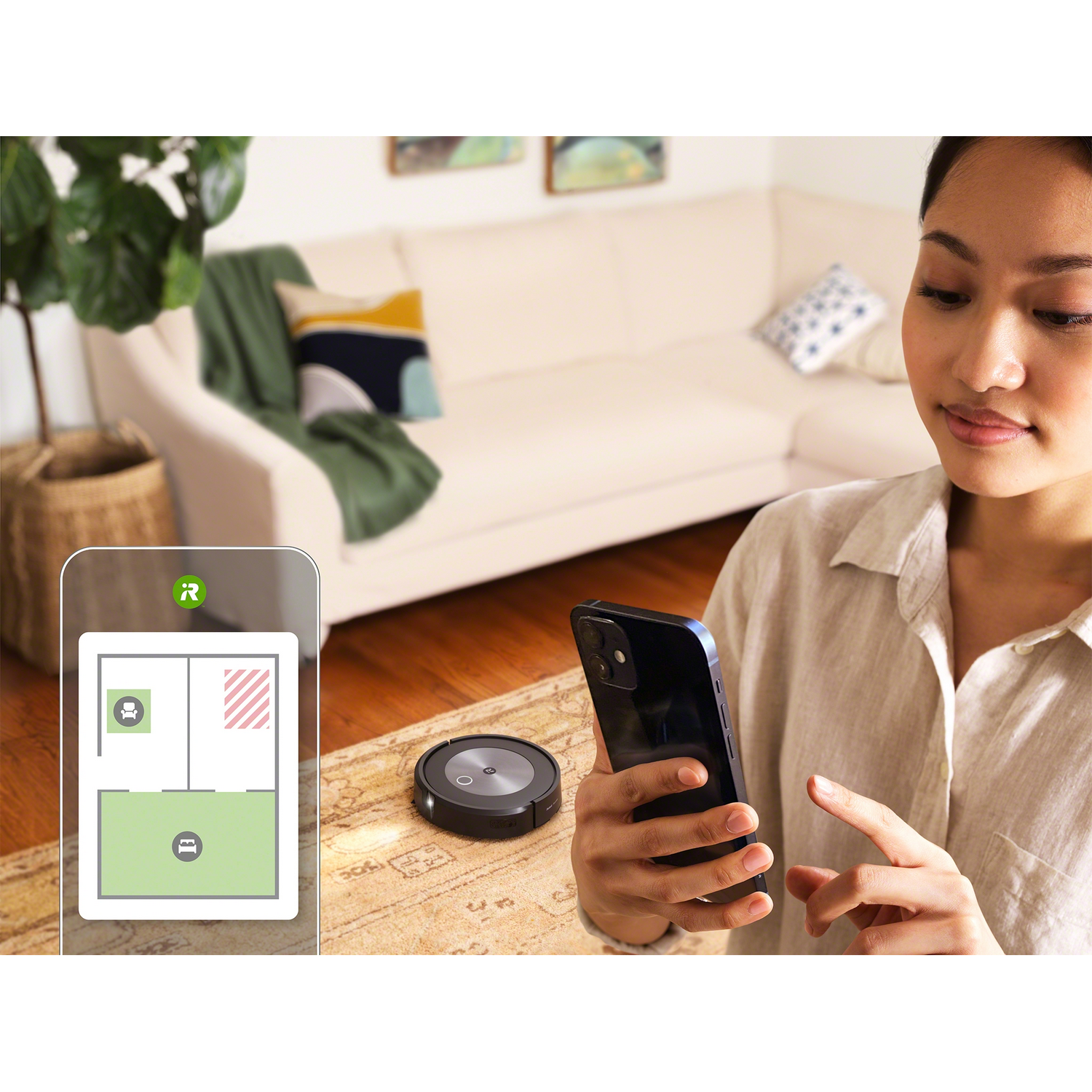 Una mujer usa un teléfono para controlar una aspiradora robot. Un plano de planta de una habitación está en el teléfono.