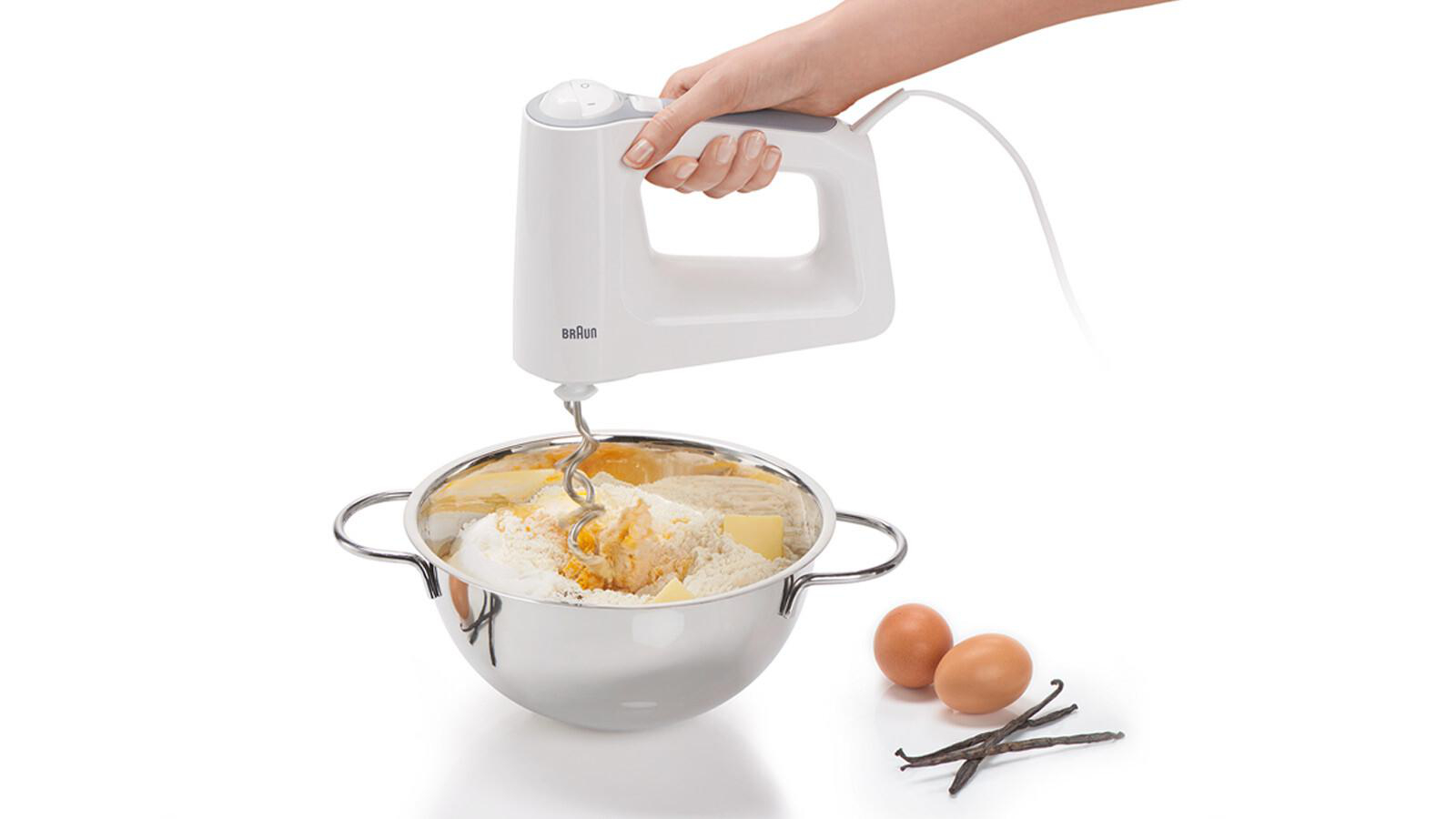 Handmixer über einer Schüssel. Zutaten: Mehl, Butter und Eier. Zusätzliche Vanilleschoten.