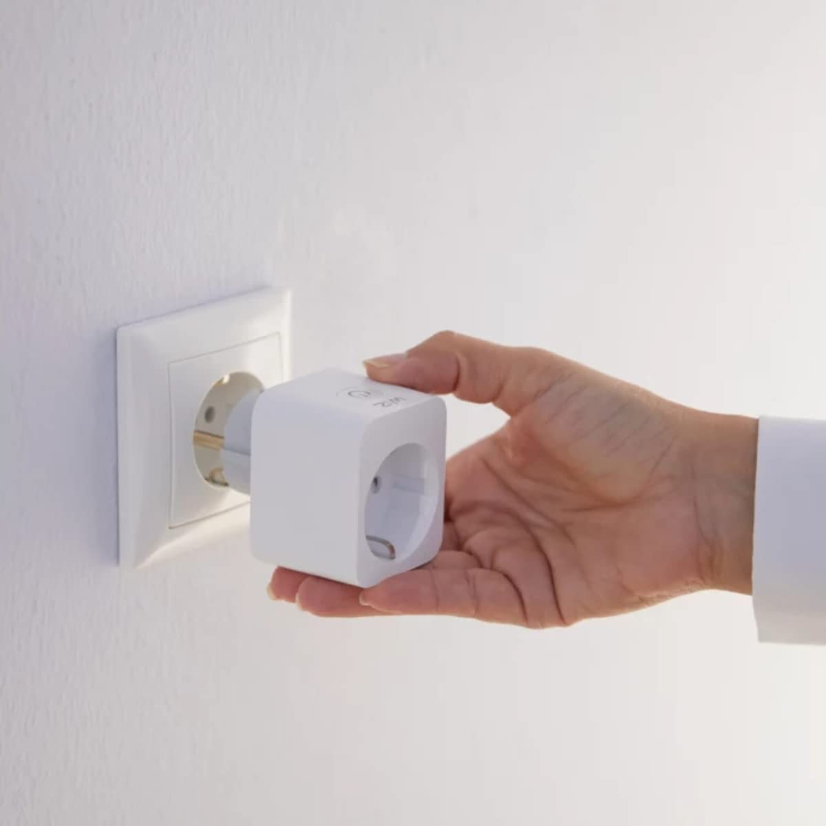 Mano insertando un enchufe inteligente blanco en una toma de corriente en una pared blanca.