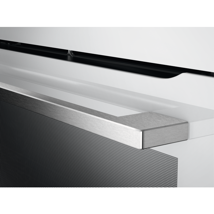 Primer plano de una manija plateada de puerta de horno y el borde superior de un horno blanco.