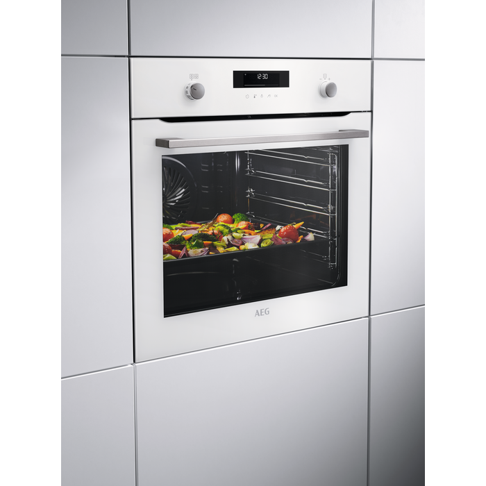 Un horno AEG con exterior blanco, la puerta abierta revela una bandeja de verduras asadas.