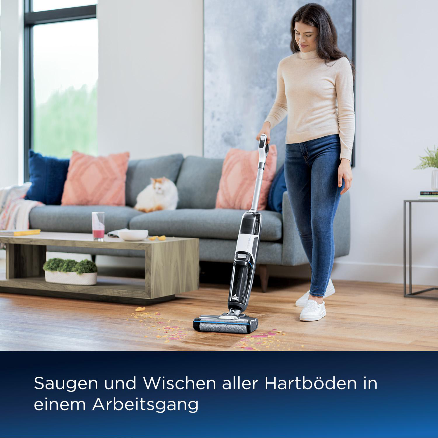Eine Frau saugt einen Holzboden. Im Hintergrund sind ein graues Sofa und eine weiße Katze zu sehen. Der Staubsauger ist schwarz-weiß.
