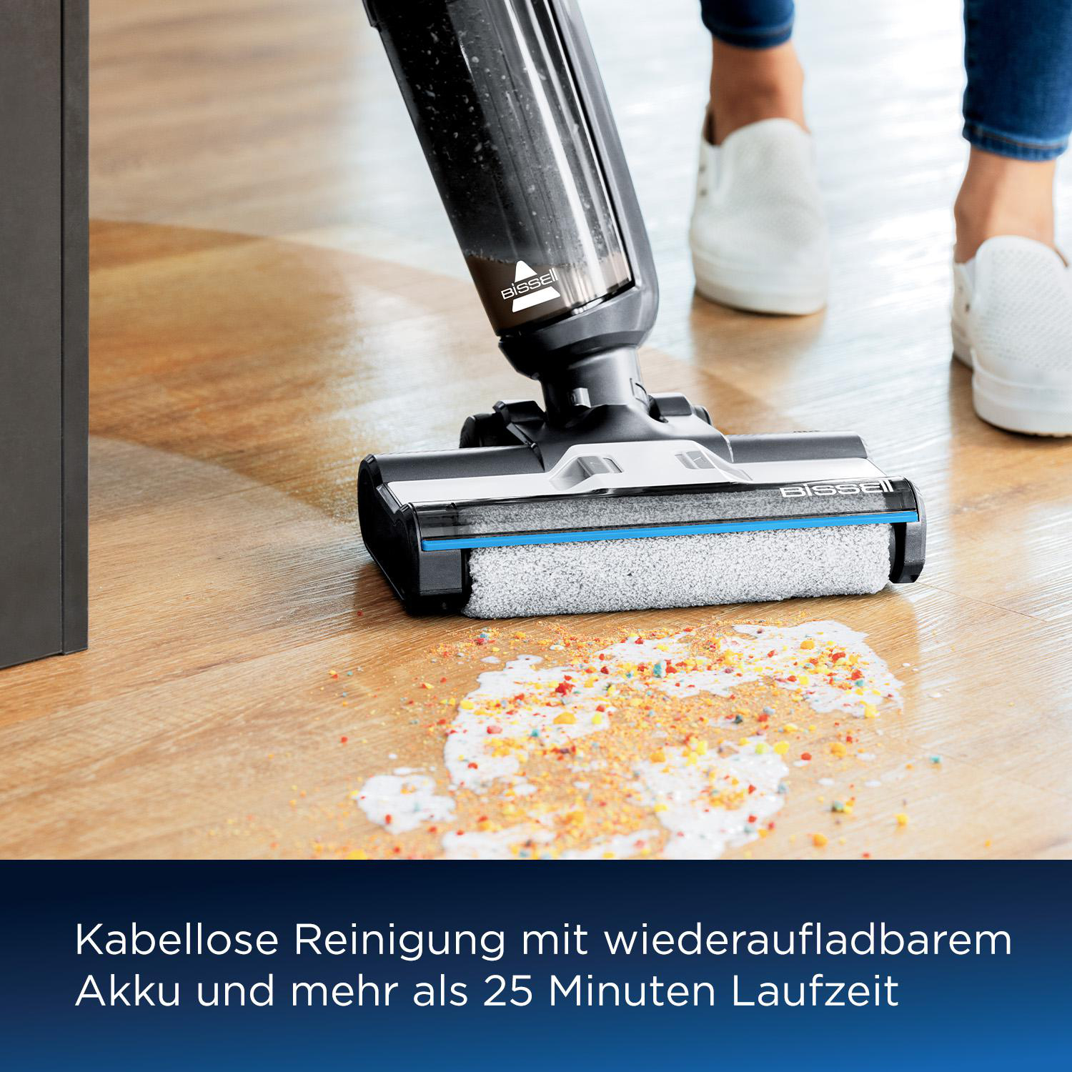 Eine Person benutzt einen Staubsauger auf einem Holzboden. Der Staubsauger ist auf einem Fleck mit bunten Ablagerungen.