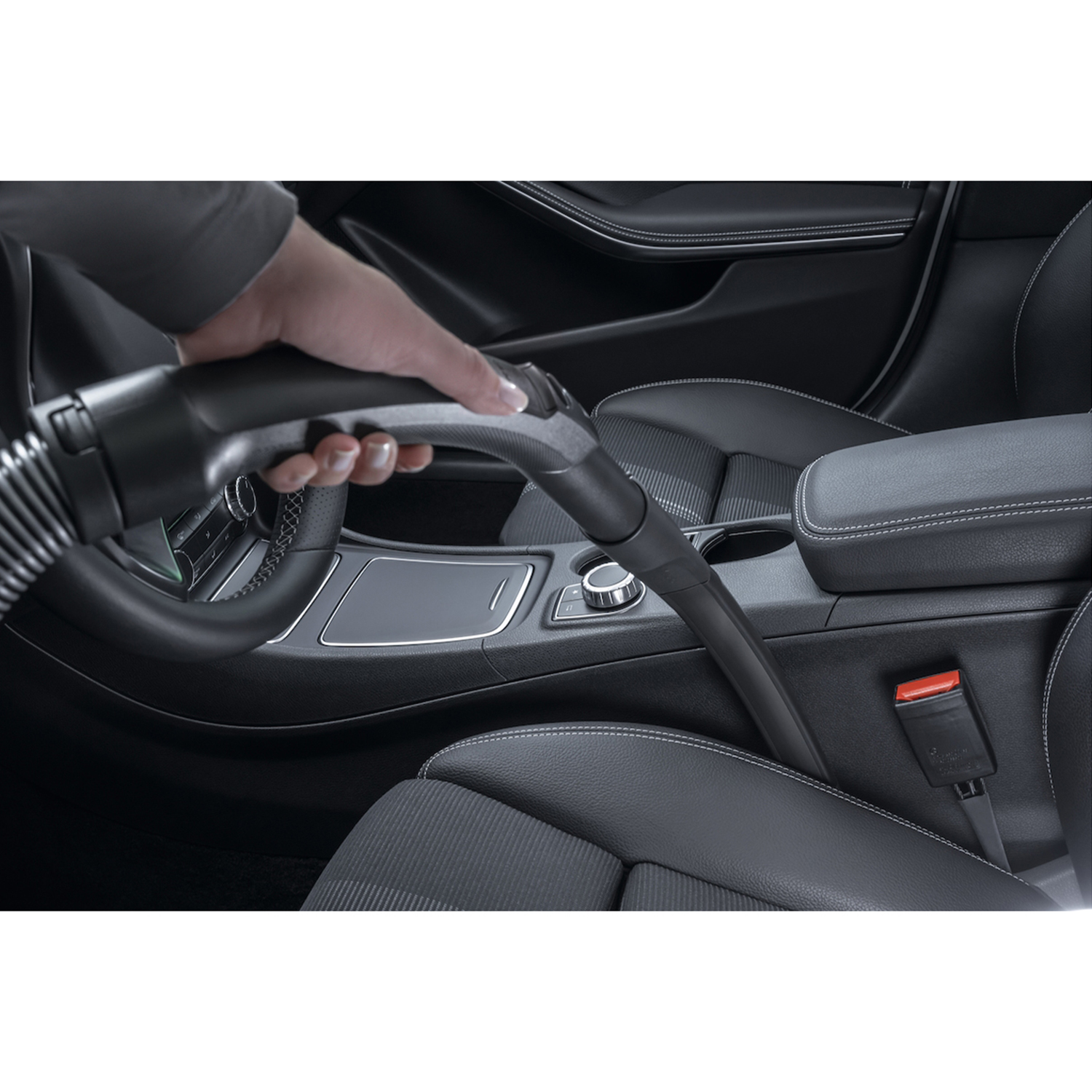 Aspirare a mano un interno auto, pulendo un sedile con l'ugello.