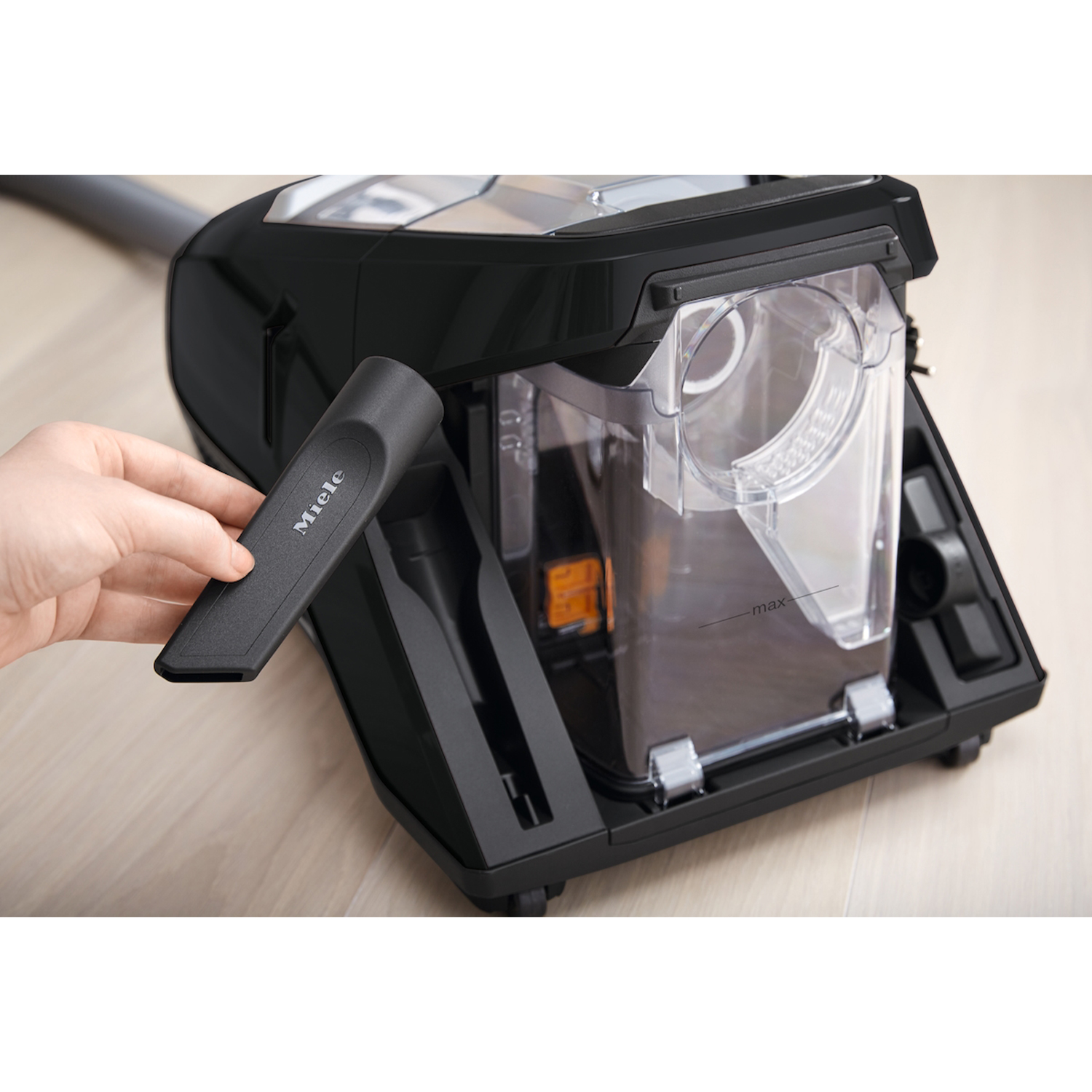 Mano che tiene l'accessorio dell'aspirapolvere Miele. Componenti dell'aspirapolvere in plastica nera e trasparente visibili.