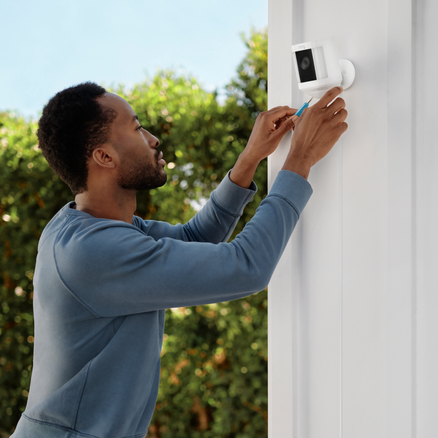 Un homme installant une caméra de sécurité blanche sur un mur avec un tournevis bleu.