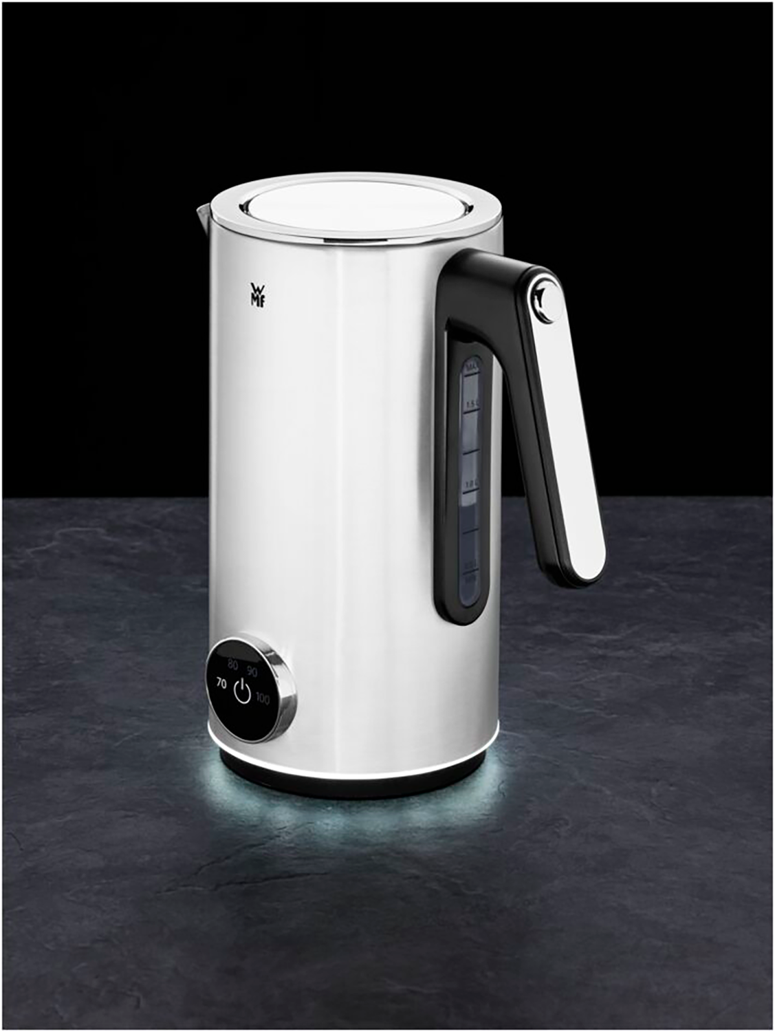 A silver and black kettle with black handle, on a black surface, with a light glowing underneath.