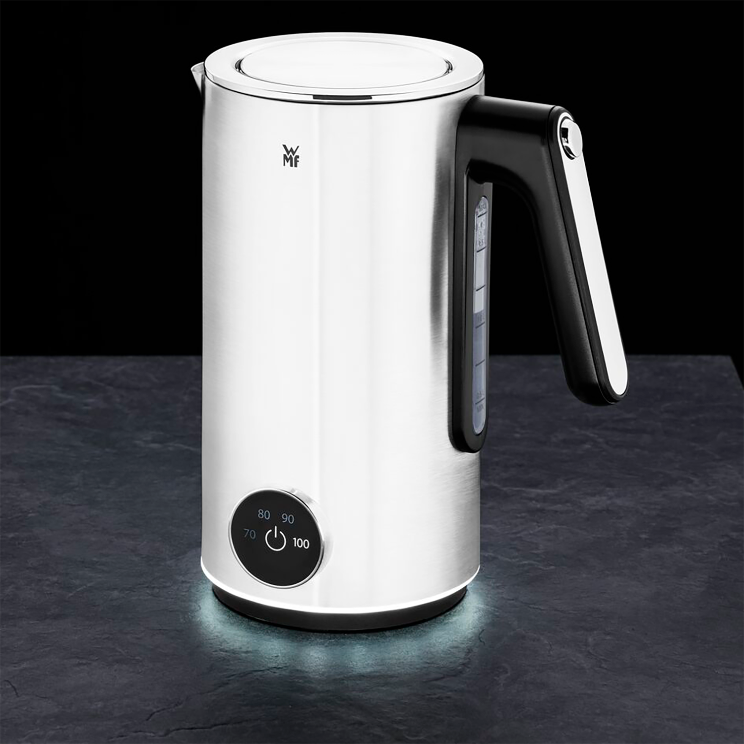 A stainless steel WMF electric kettle with a black handle and controls. It is on a dark surface.