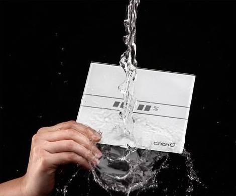 Kéz, amely egy fehér panelt tart, amelyet víz fröcsköl. Fekete háttér.
