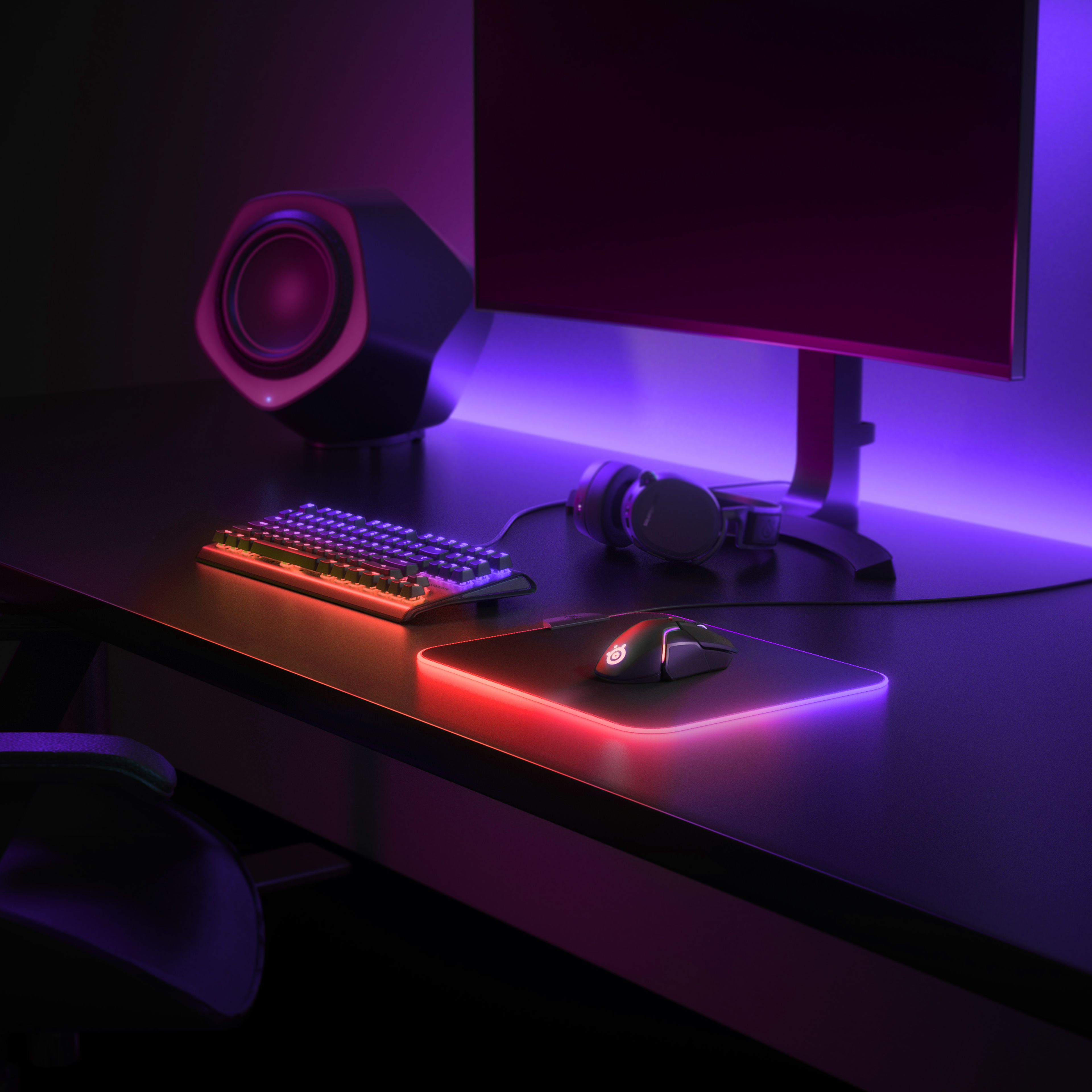 Neon ışıklarla aydınlatılmış, monitör, klavye, fare ve hoparlörlü oyun kurulumu.