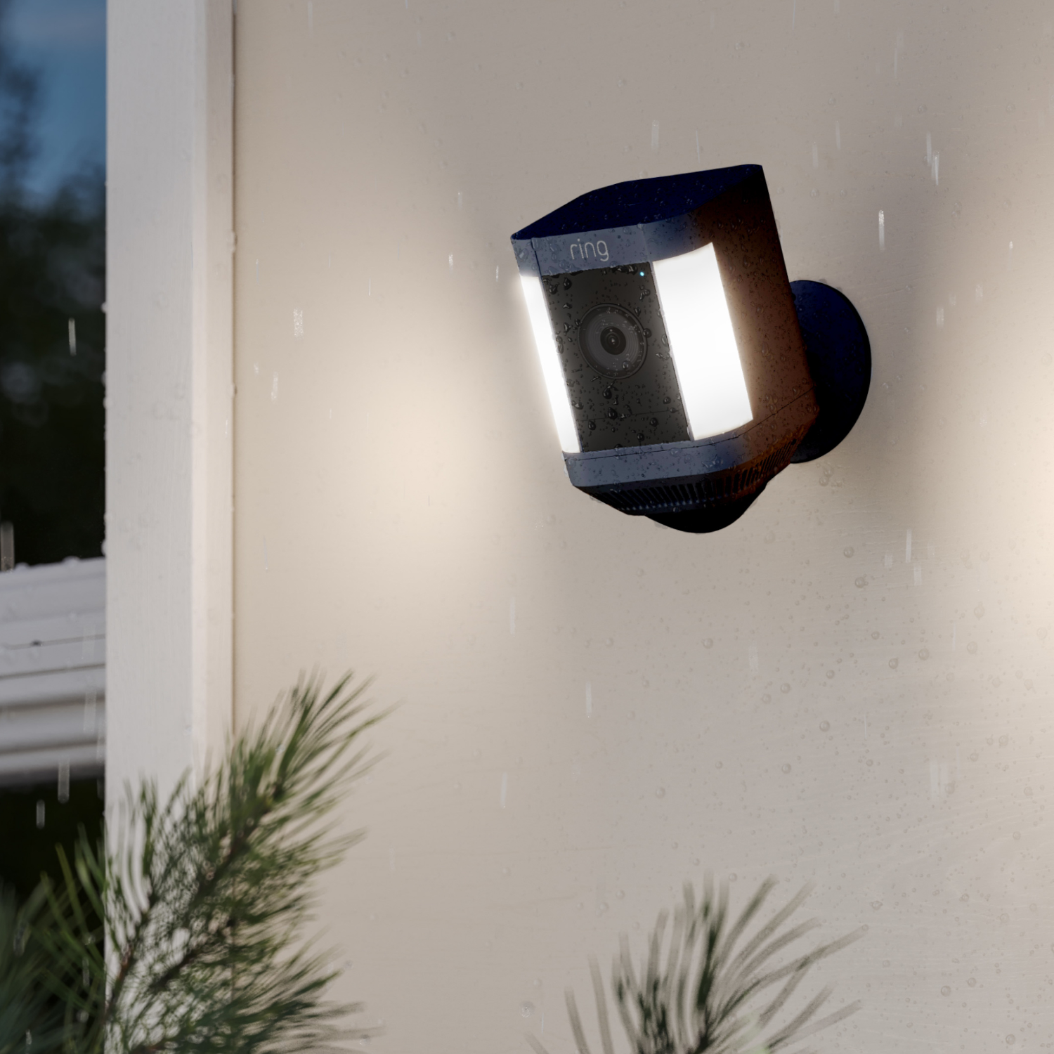 Een Ring-beveiligingscamera gemonteerd op een muur tijdens de regen, gericht op de kijker, met licht aan.