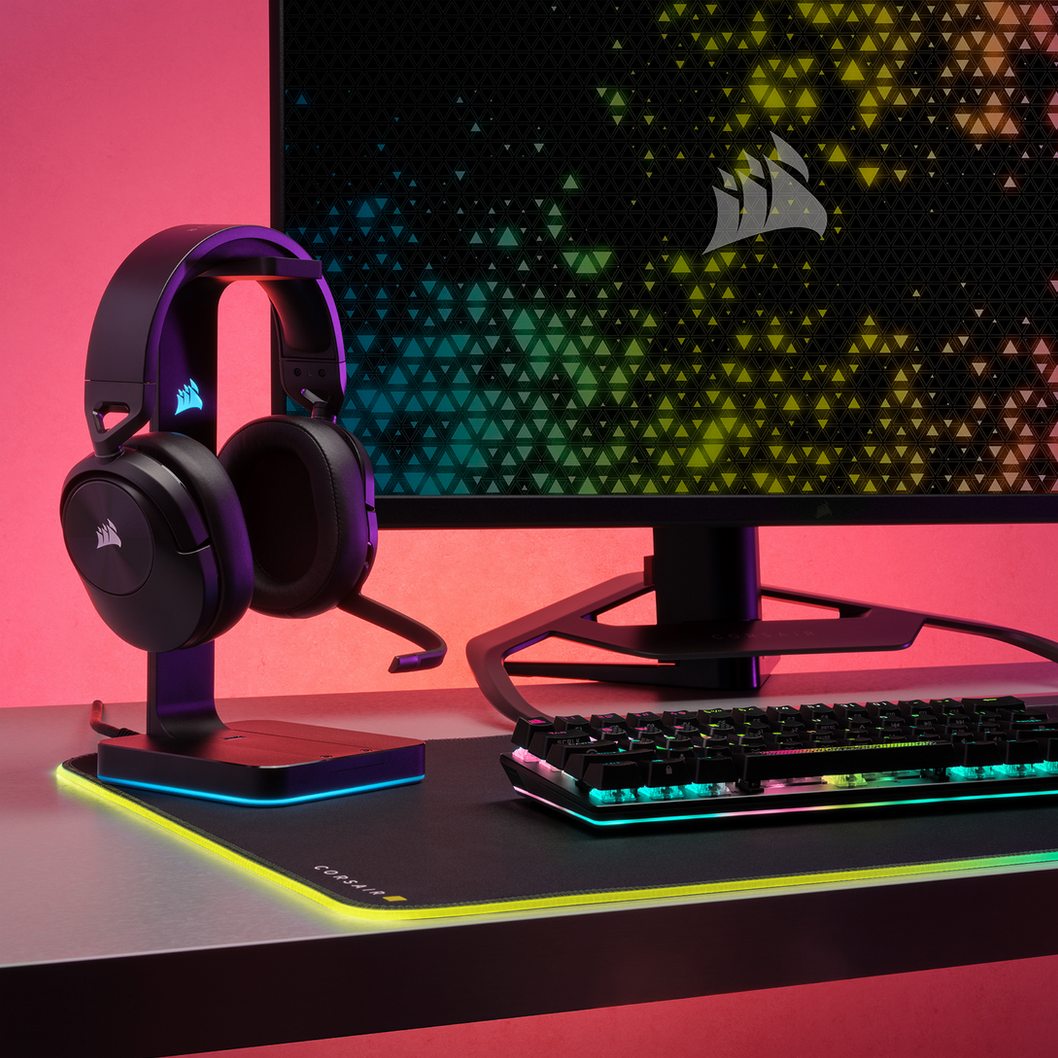 Zwarte headset op standaard, monitor en toetsenbord op bureau, roze achtergrond.
