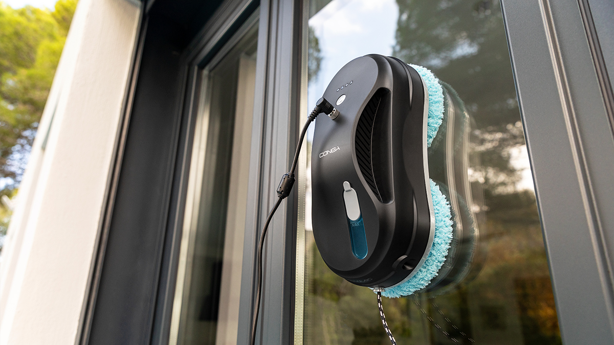Robot limpiador de ventanas negro en una ventana, con almohadilla de limpieza azul. Fondo brillante.