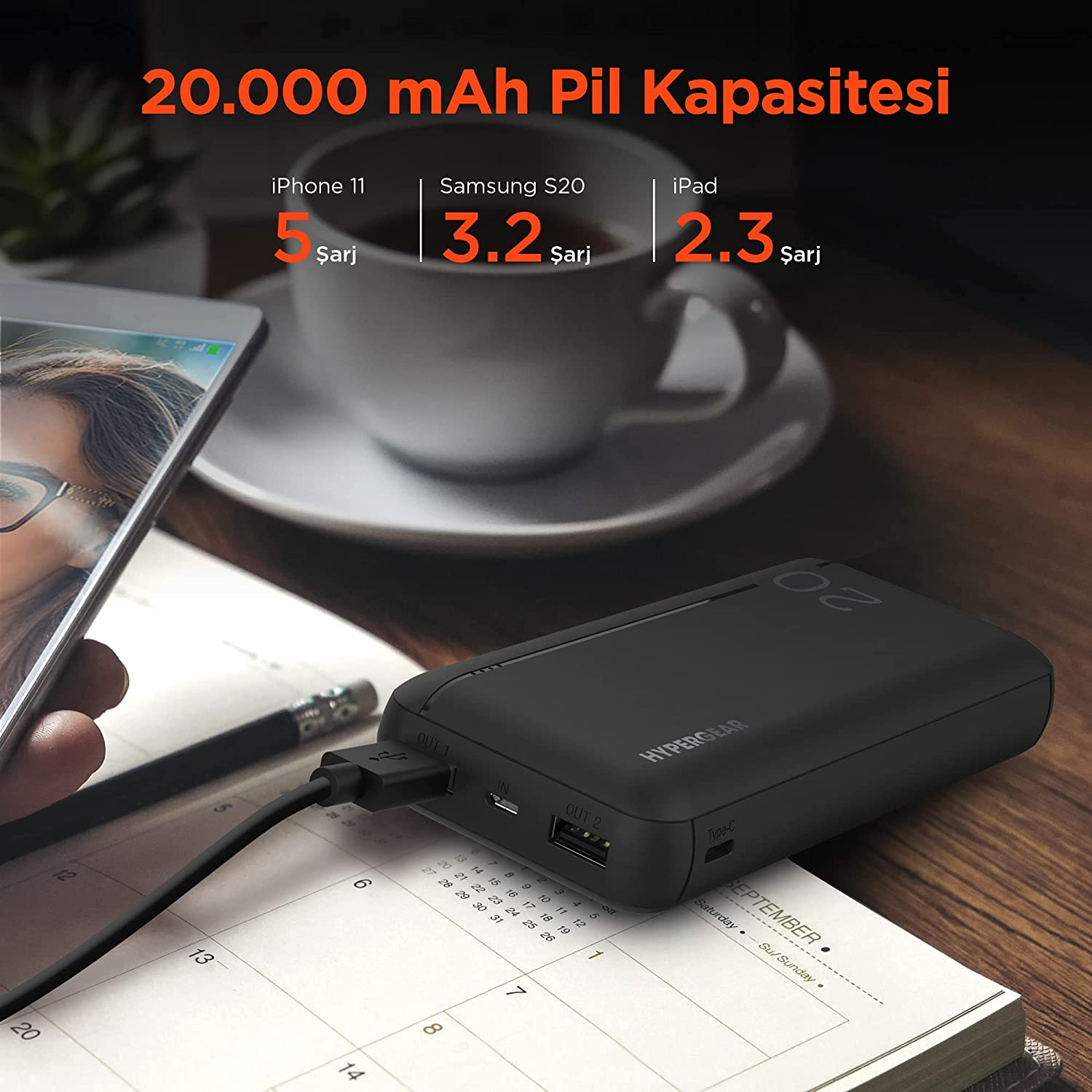 Siyah powerbank bir telefonu şarj ediyor. Ahşap masada beyaz kupa ve kalem.